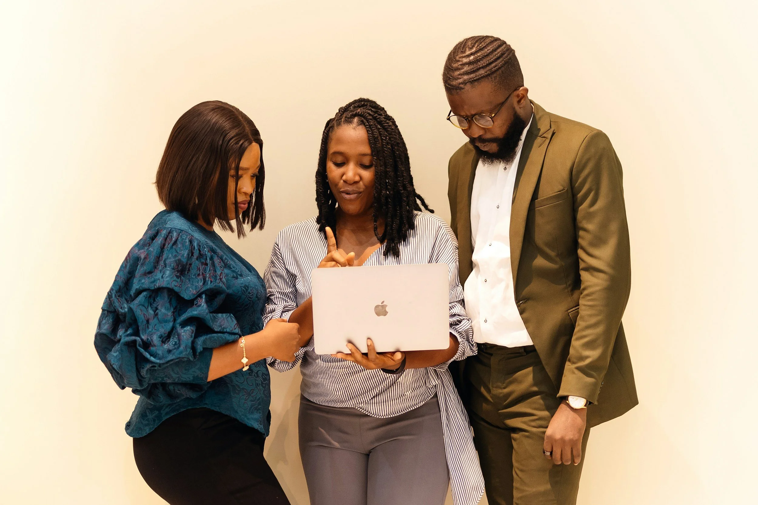 Three people, two women and one man, are looking at a laptop screen together. They appear engaged and focused on what is displayed.