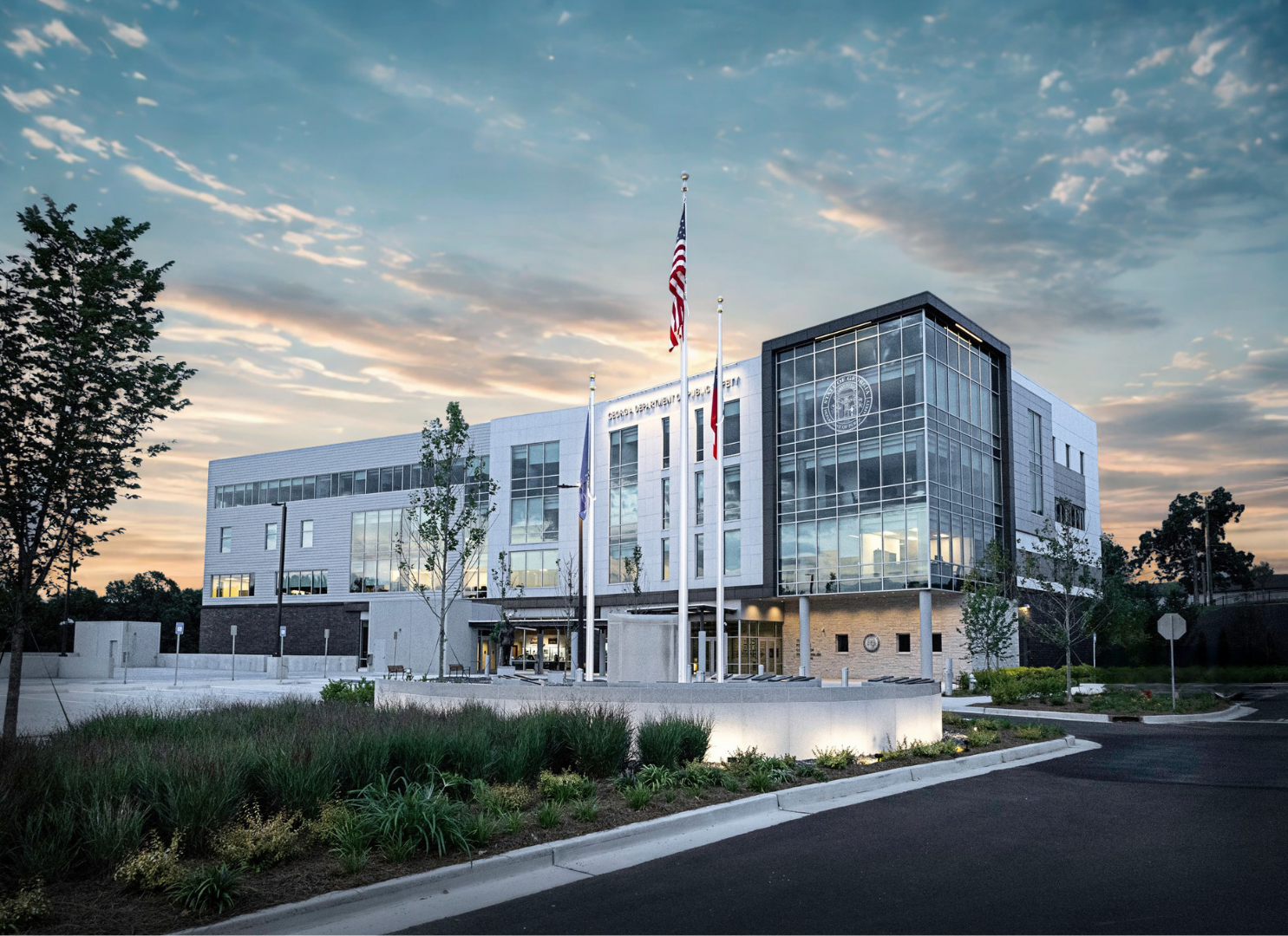 Modern government building with glass windows, flags, and landscaped surroundings during early evening or late afternoon.