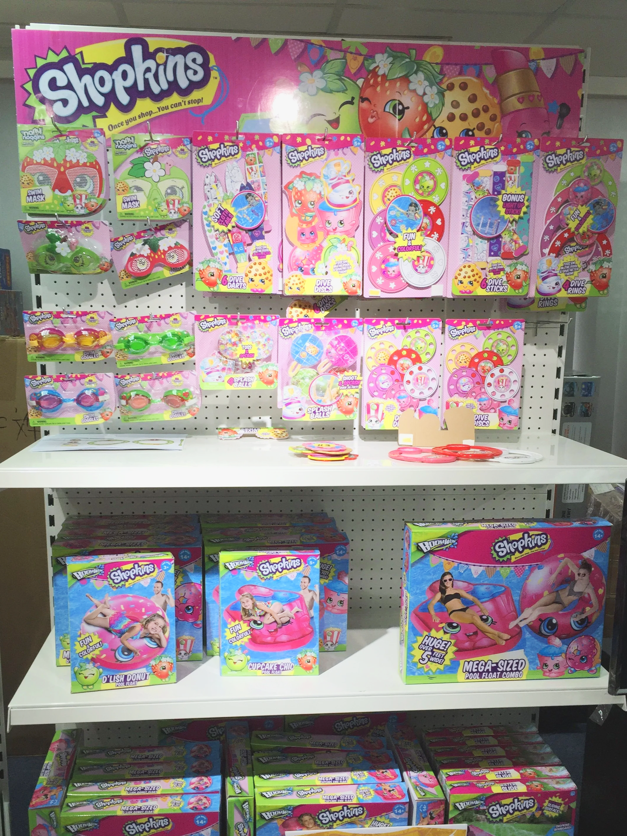 Display of colorful Shopkins-themed pool float toys and accessories on retail shelves, featuring packaging with children and bright, playful designs.