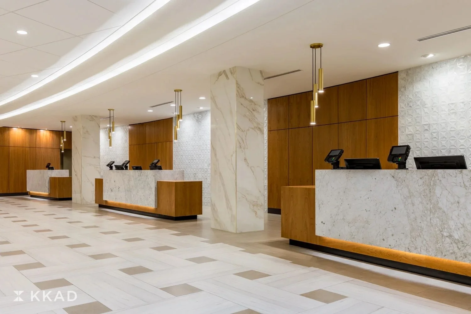 Modern hotel check-in counter with multiple reception desks made of marble and wood, illuminated by pendant lights, with a polished tile floor and decorative wall panels.