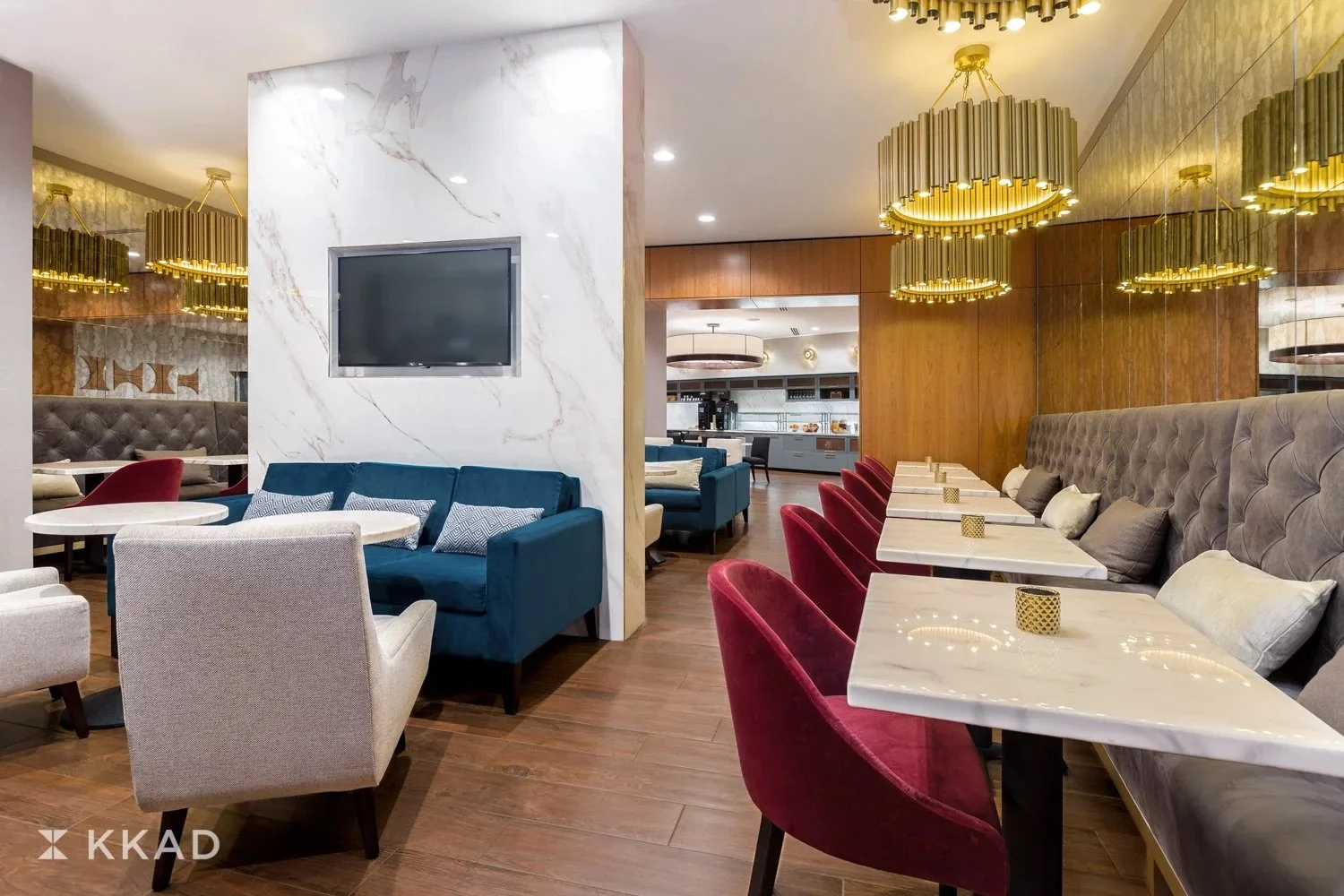 Interior of a modern restaurant with colorful seating, marble tables, gold chandeliers, and a wood-paneled wall.