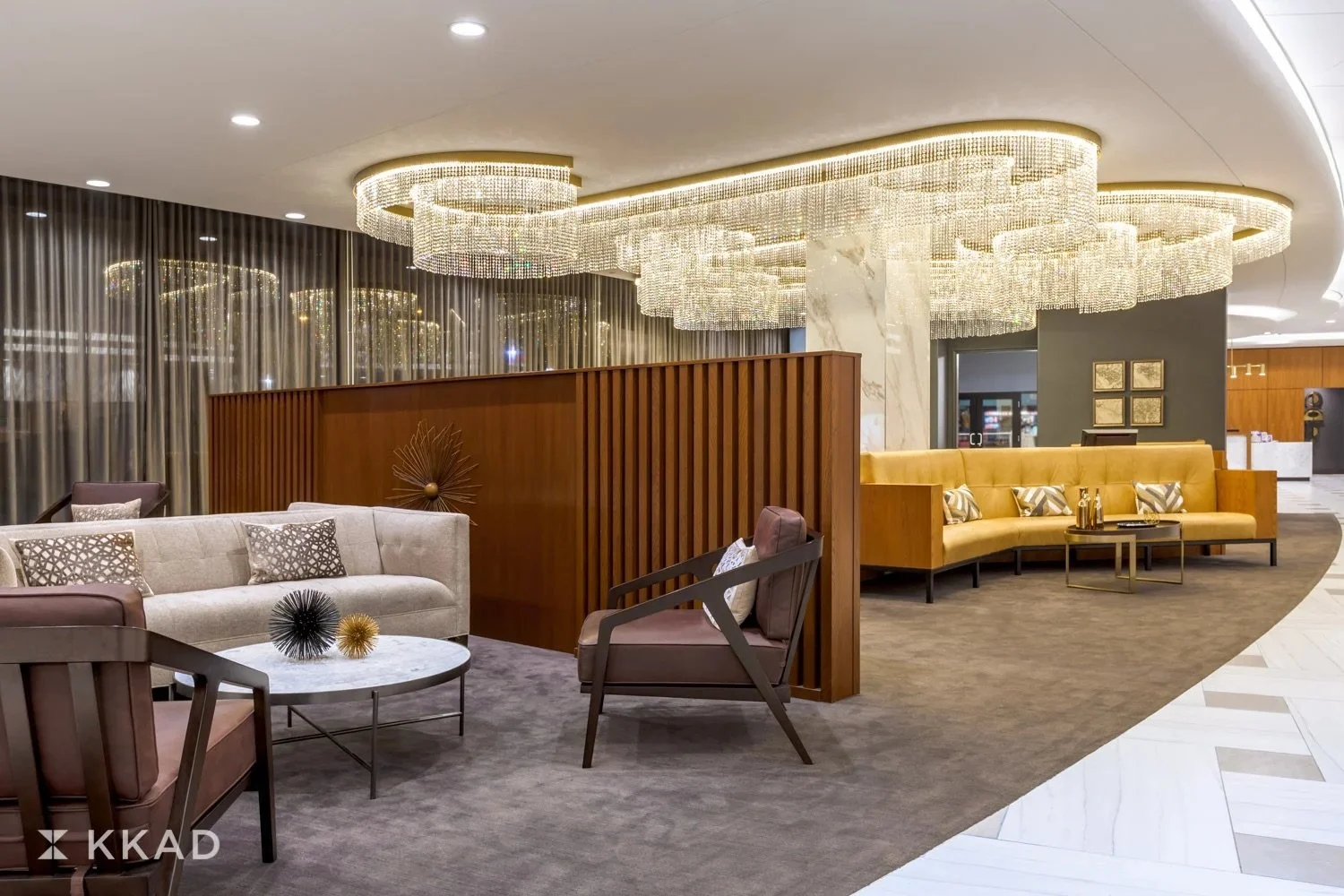 Modern hotel lobby with luxurious chairs, sofas, and a chandelier. Gold and marble accents, wood paneling, and curtains create an elegant ambiance.