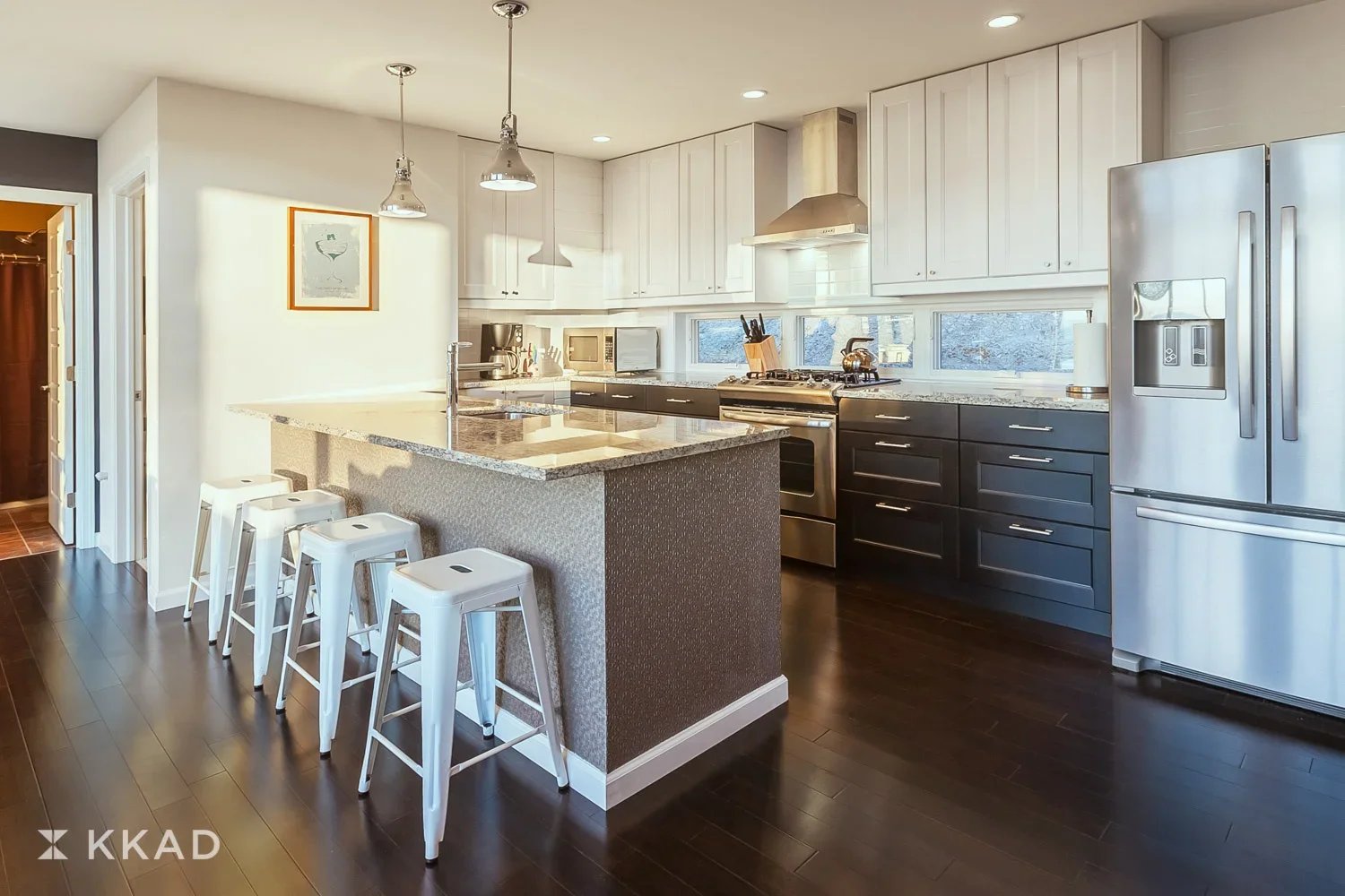 Modern kitchen with white upper cabinets, black lower cabinets, a large granite island, stainless steel appliances, and dark hardwood floors.