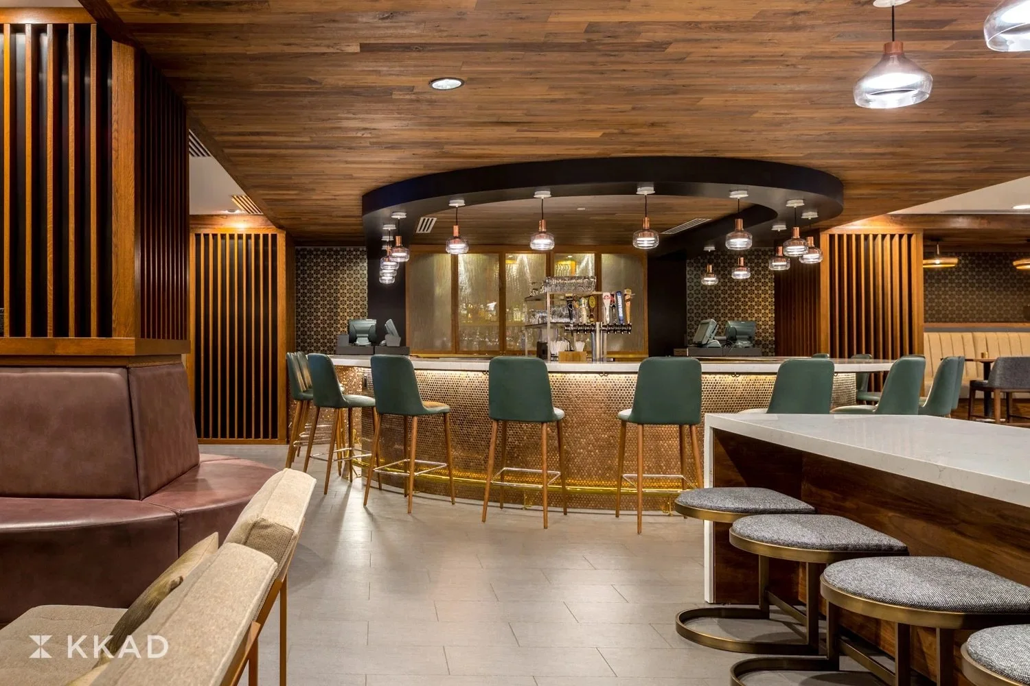 Interior of a modern bar with a curved counter, green barstools, and ambient lighting.