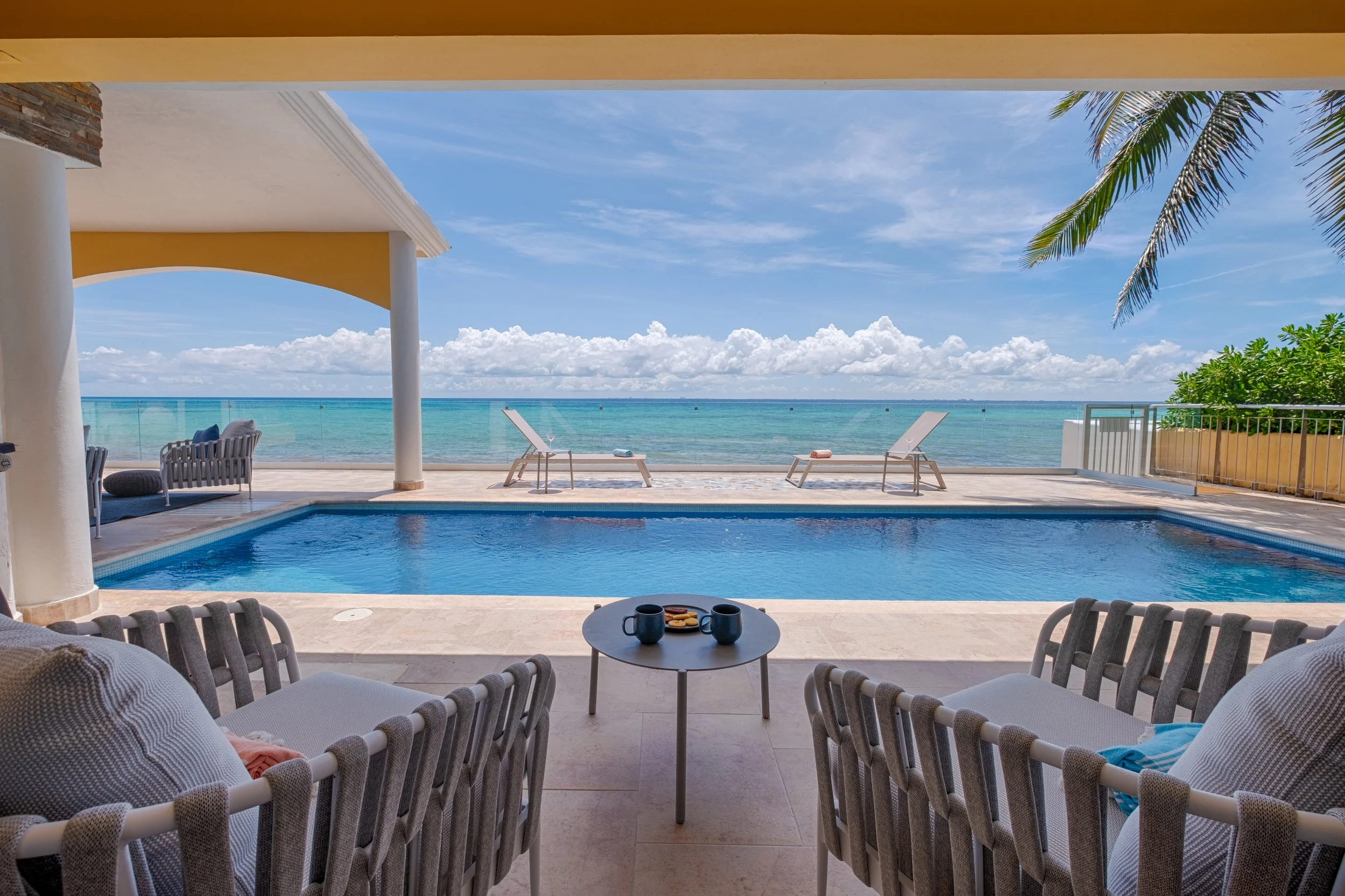 Poolside seating area overlooking ocean with lounge chairs and palm tree