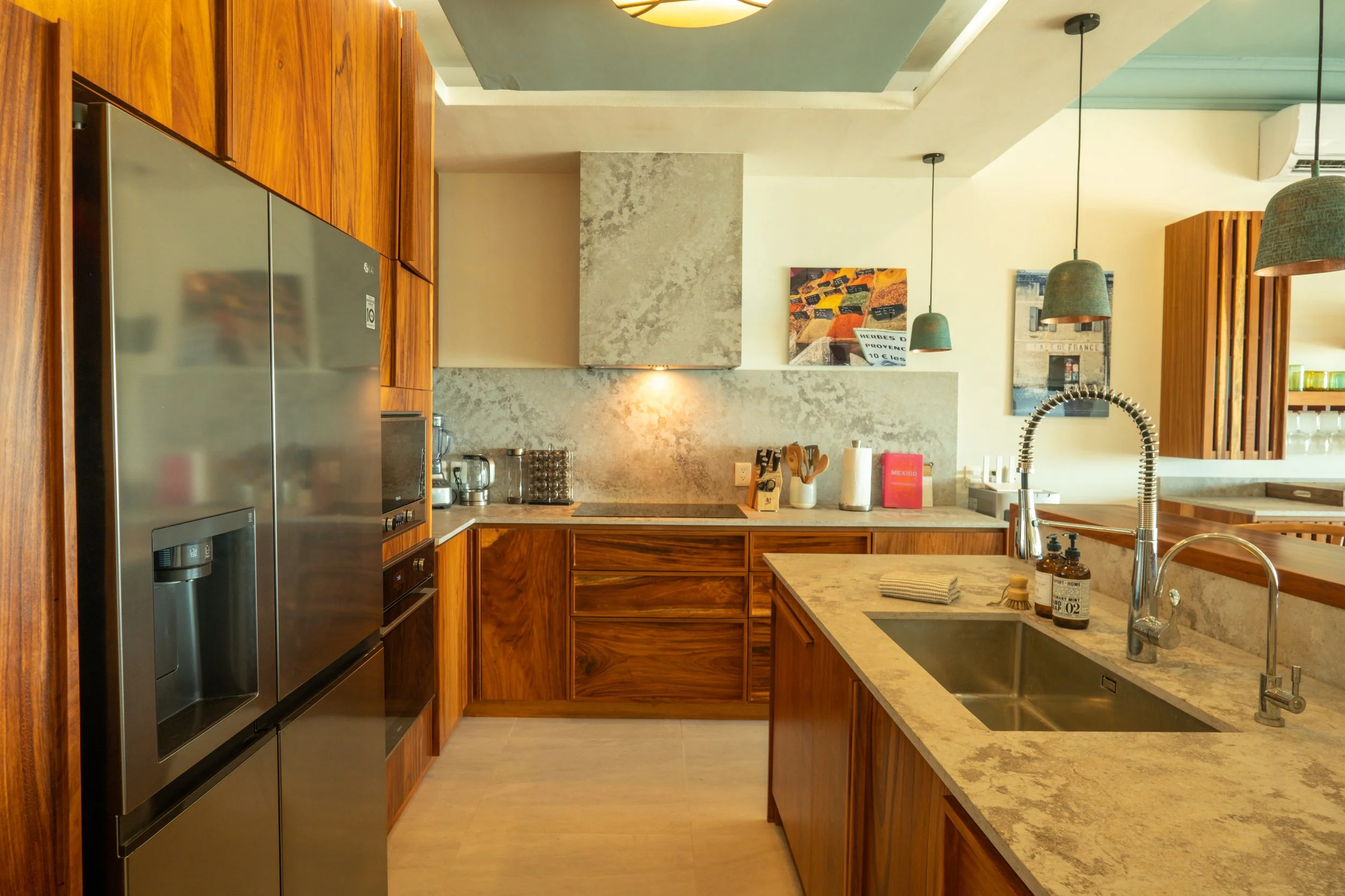 Modern kitchen with wooden cabinets, marble countertops, stainless steel appliances, and pendant lights.