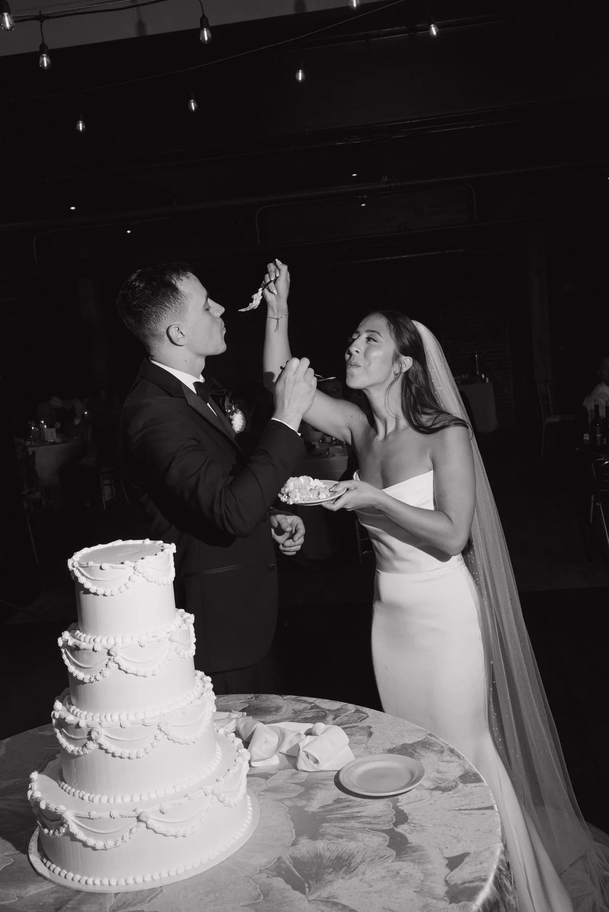 A newlywed couple sharing a playful cake-cutting moment at their reception, captured in moody black and white, the kind of unforgettable memory Palm Events & Rentals helps create for couples and their guests.
