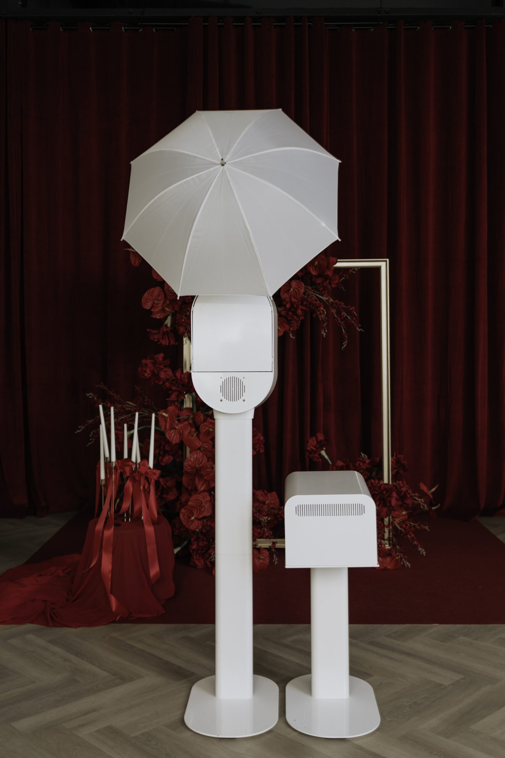 A sleek white photo booth setup against a dramatic red curtain backdrop, the kind of fun, memorable entertainment Palm Events & Rentals brings to weddings and events.