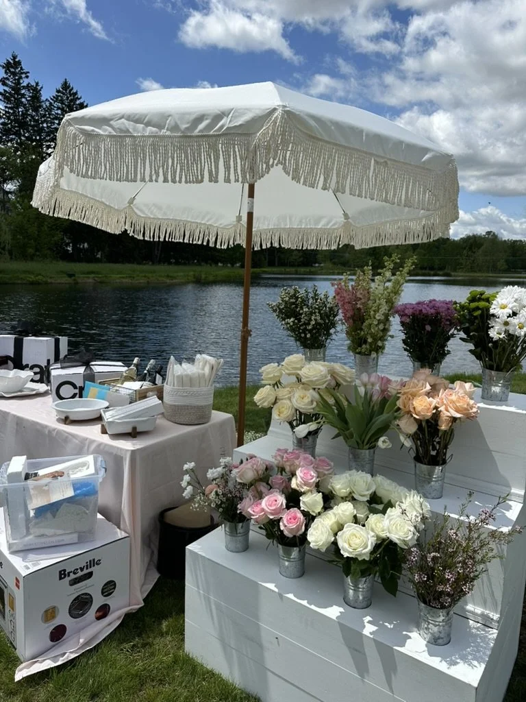 A lush make-your-own bouquet station with fresh florals in every color, set lakeside under a fringed white umbrella, the kind of interactive, Instagram-worthy moment Palm Events & Rentals designs to delight every guest.