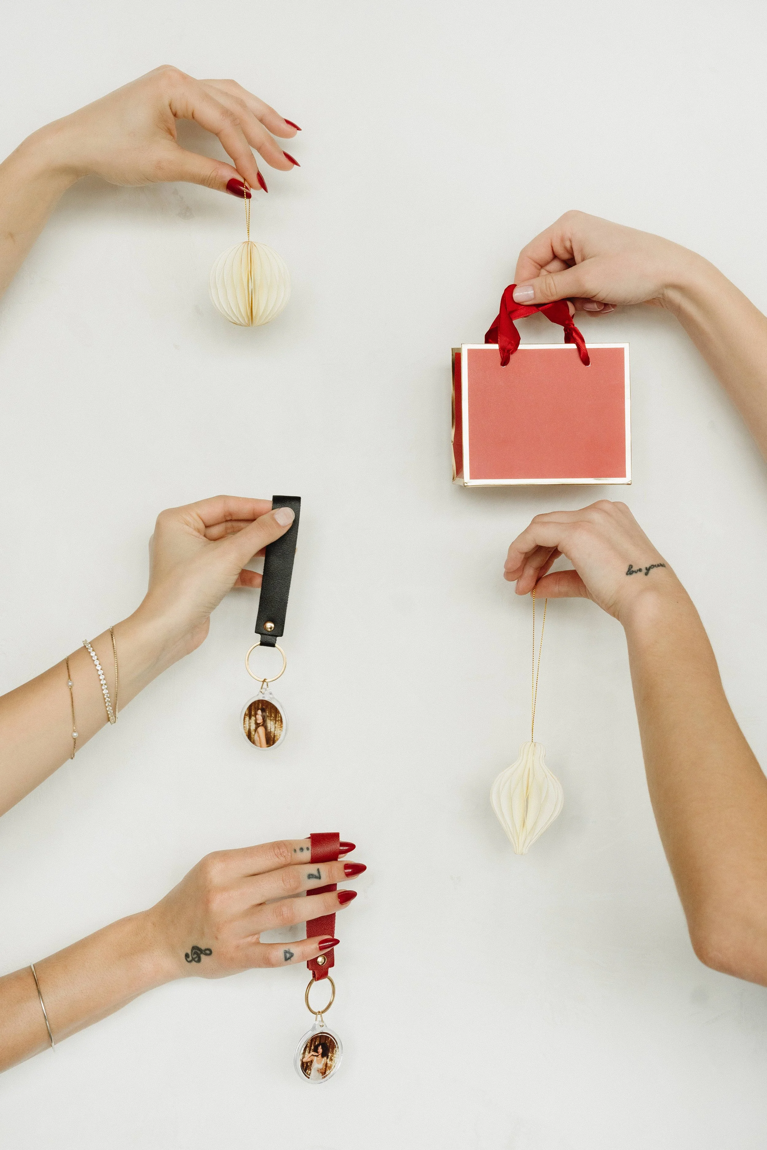 Hands with red nails arranging jewelry, ornaments, and a gift bag on a clean white surface, the kind of thoughtful gifting moment Palm Events & Rentals can curate for your wedding or next event.