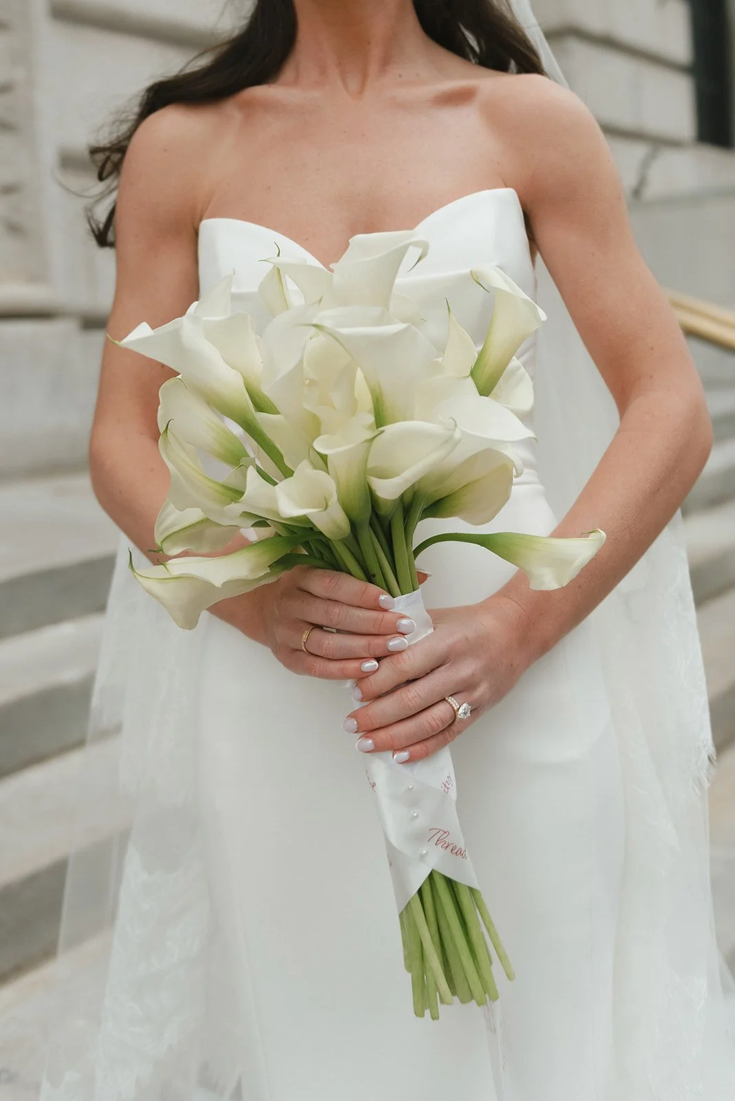 A woman in a wedding dress holding a bouquet of white calla lilies.