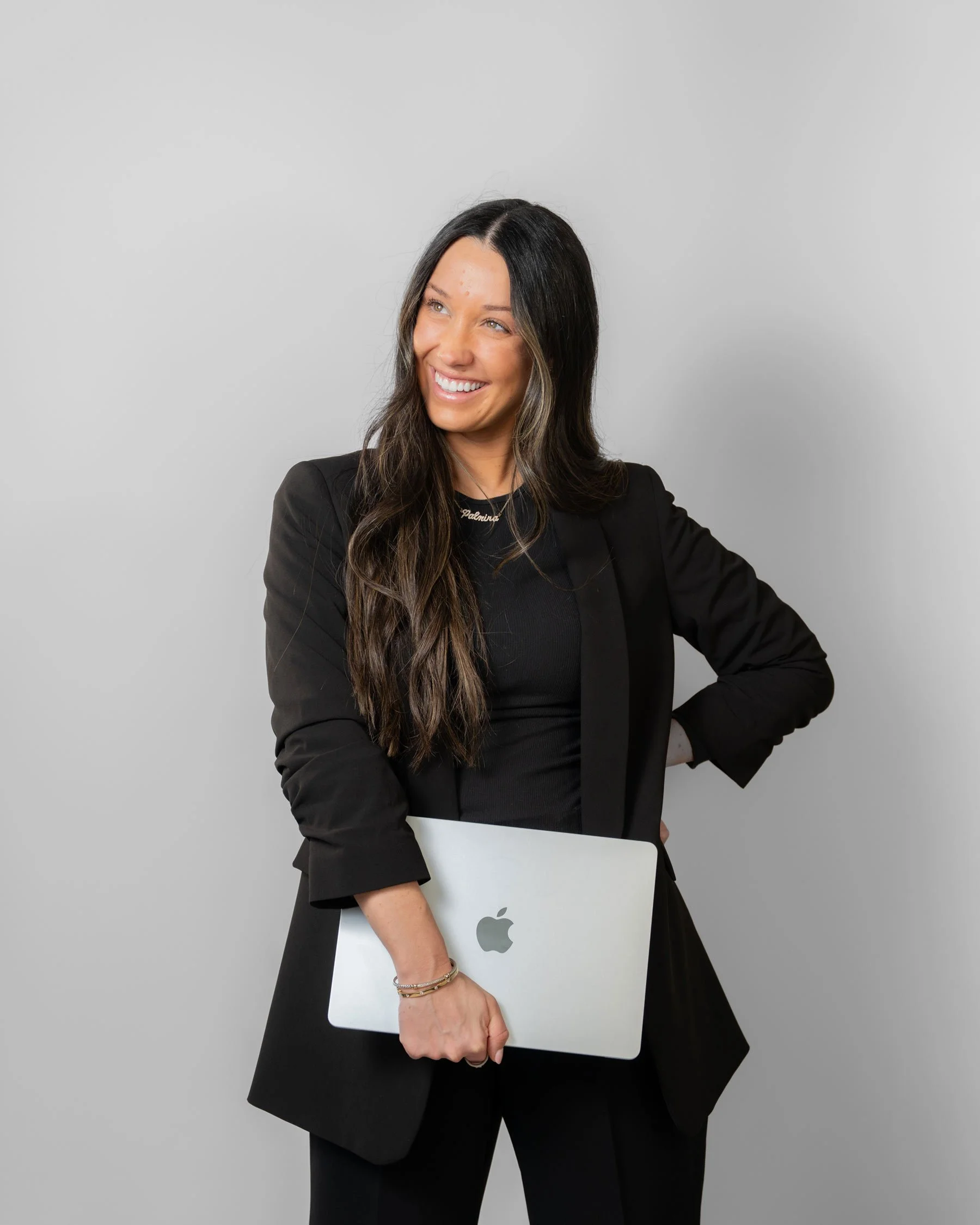 Rachel Smith, owner of Palm Events & Rentals, smiling confidently in a black blazer and holding a MacBook, the woman behind the magic helping couples and clients bring their dream events to life.