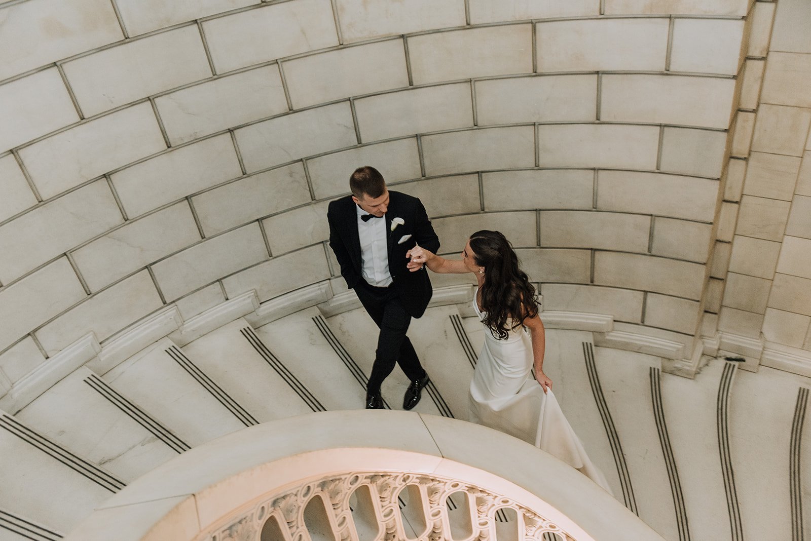A newlywed couple ascending a breathtaking spiral stone staircase, shot from above, the kind of stunning, cinematic wedding moment Palm Events & Rentals helps make possible.