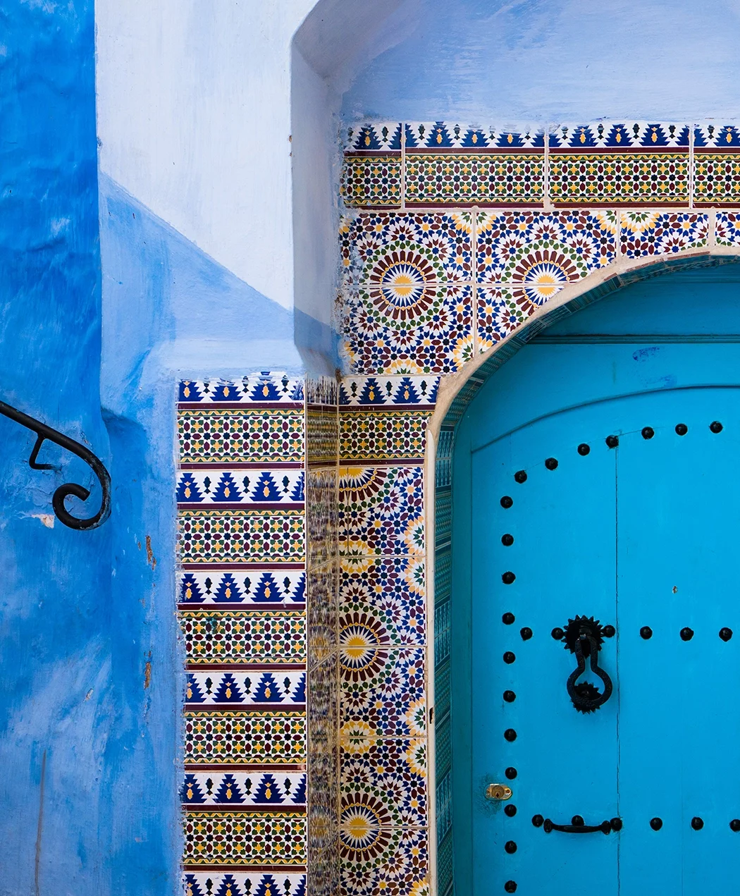 Vivid blue door with black hardware, surrounded by colorful Moroccan-style tile decorations and painted walls.