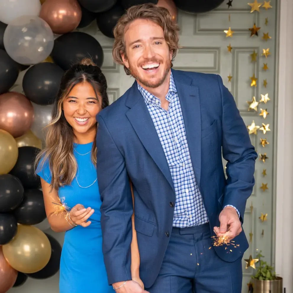 Two people smiling and celebrating in front of a backdrop of balloons and gold stars.