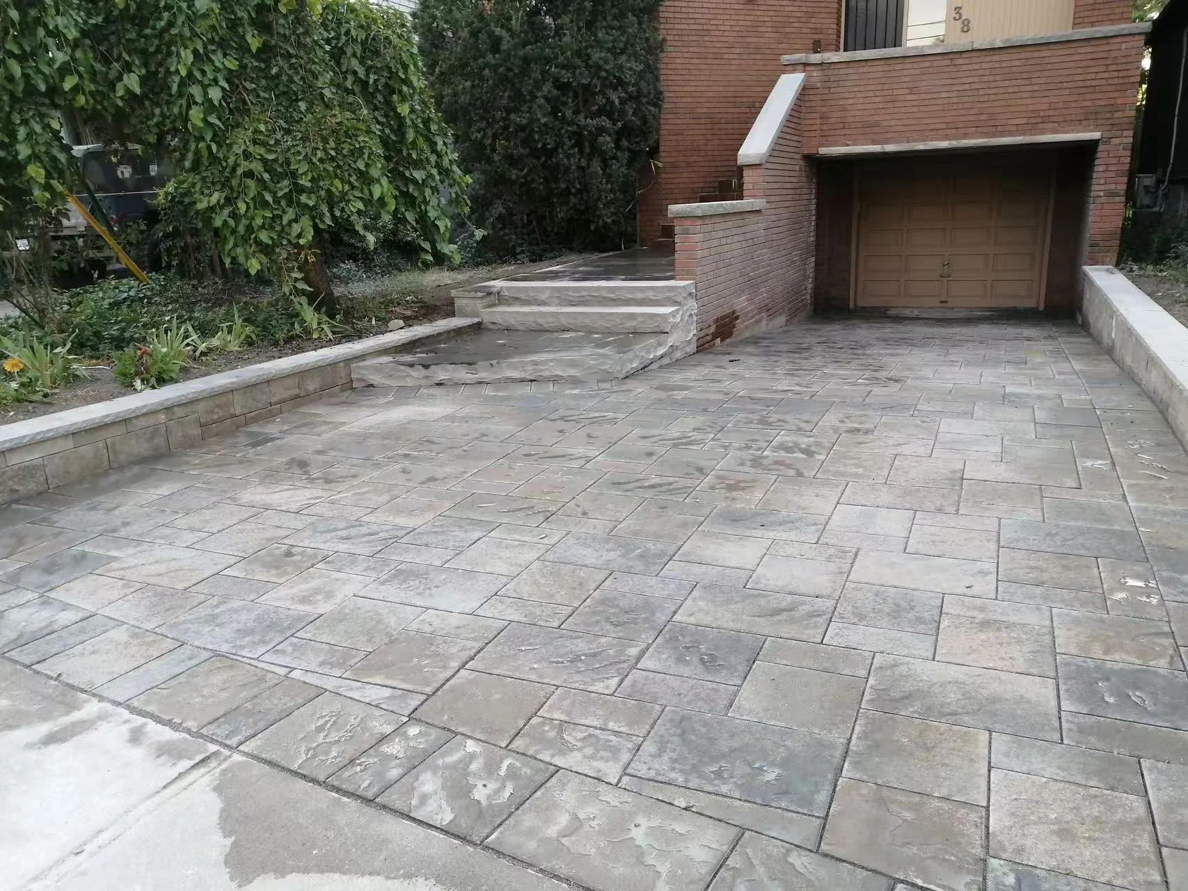 A paved driveway in front of a brick house with stairs leading up to the entrance and a garage door.