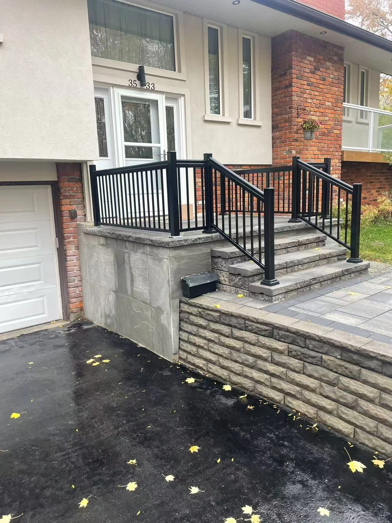 Front porch of a house with black metal railing, brick stairs, and a white door, with the house number 33 and 35 visible above the door, and a hanging flower pot on a brick column.