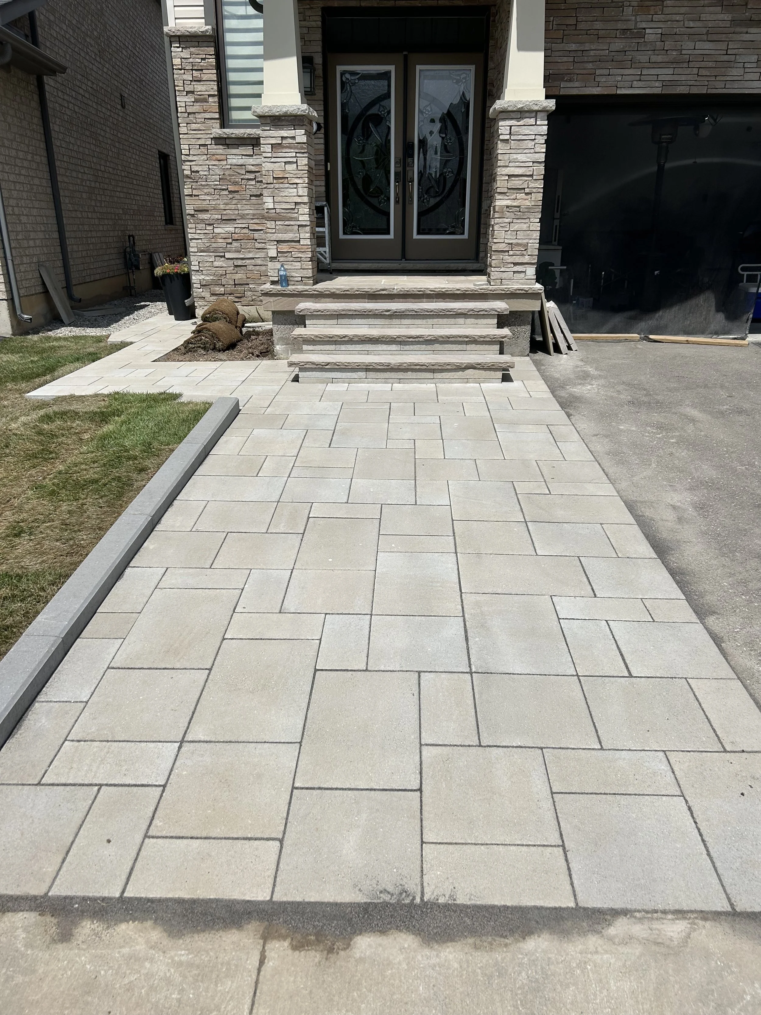 Newly paved concrete porch with steps leading up to front door of a house, with surrounding landscaping and construction materials nearby.