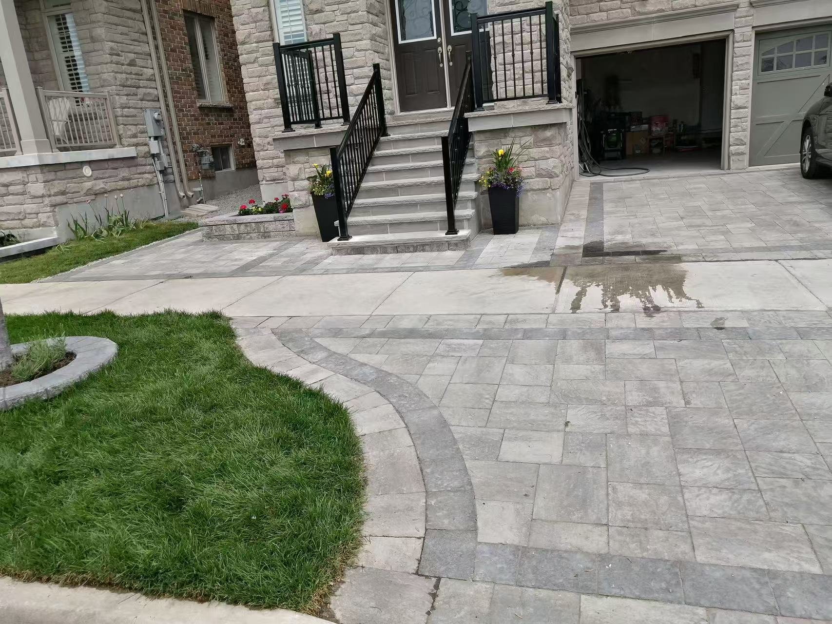 Front yard and porch of a house with stone steps, black railings, potted flowers, and a freshly cleaned driveway.