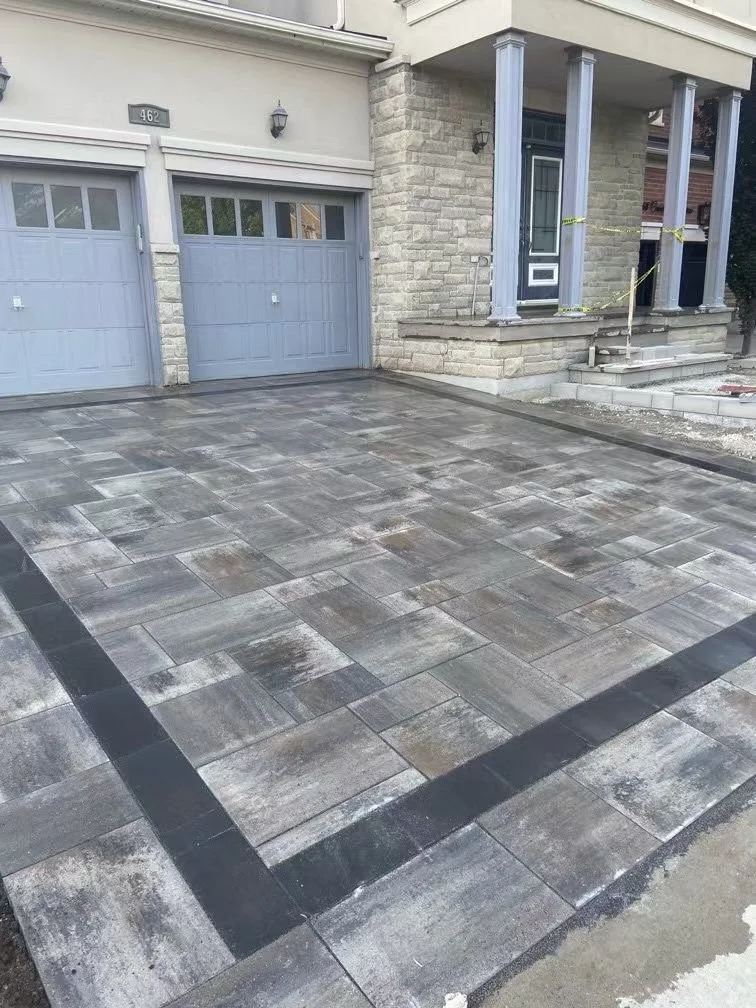 Newly installed stone driveway with a border pattern in front of a house with light blue garage doors and a porch with gray columns.