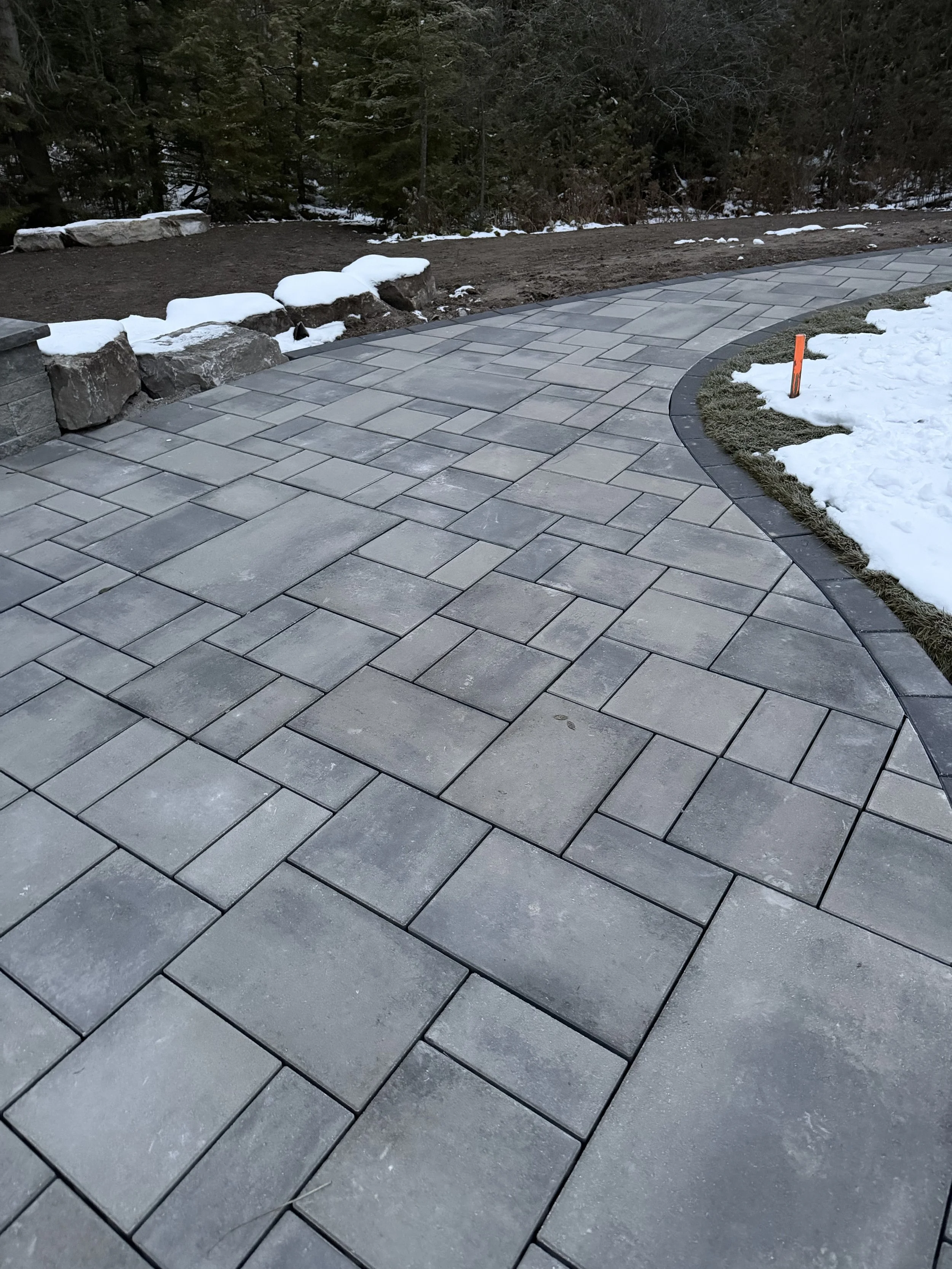 A paved walkway winding through a snowy landscape with rocks and trees in the background.