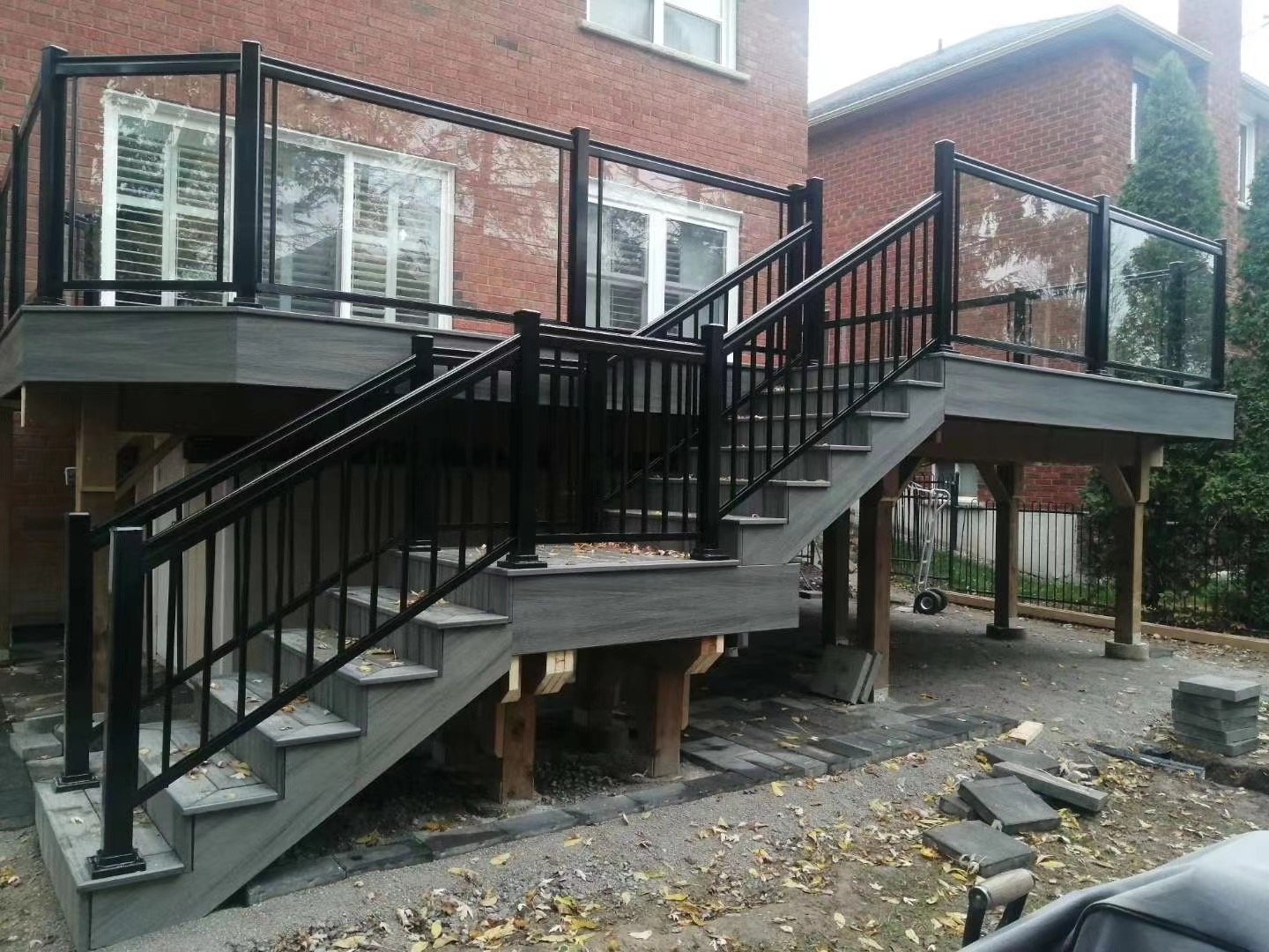 Under construction wooden deck with black metal railing attached to brick house, stairs, and outdoor space.