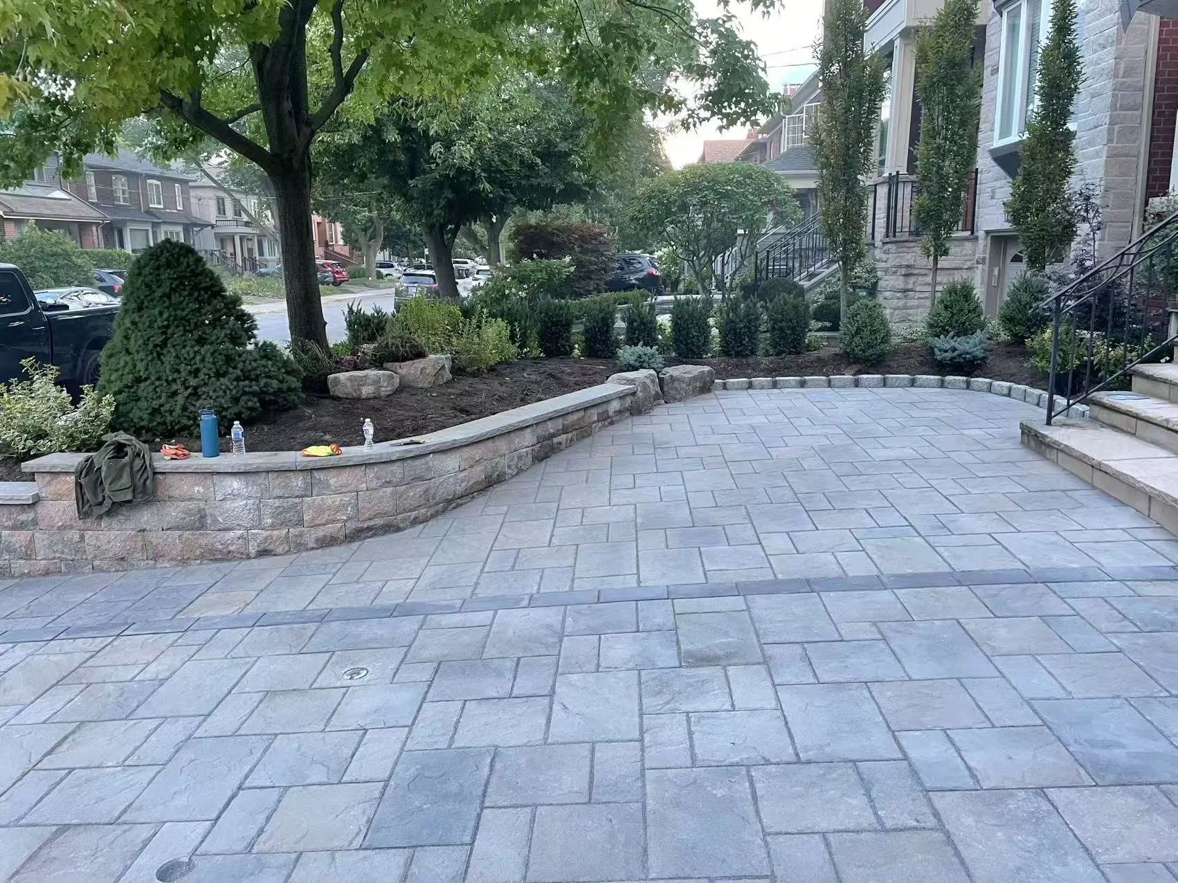 A newly paved stone patio with a low stone retaining wall and landscaped garden bed in front of a residential house.