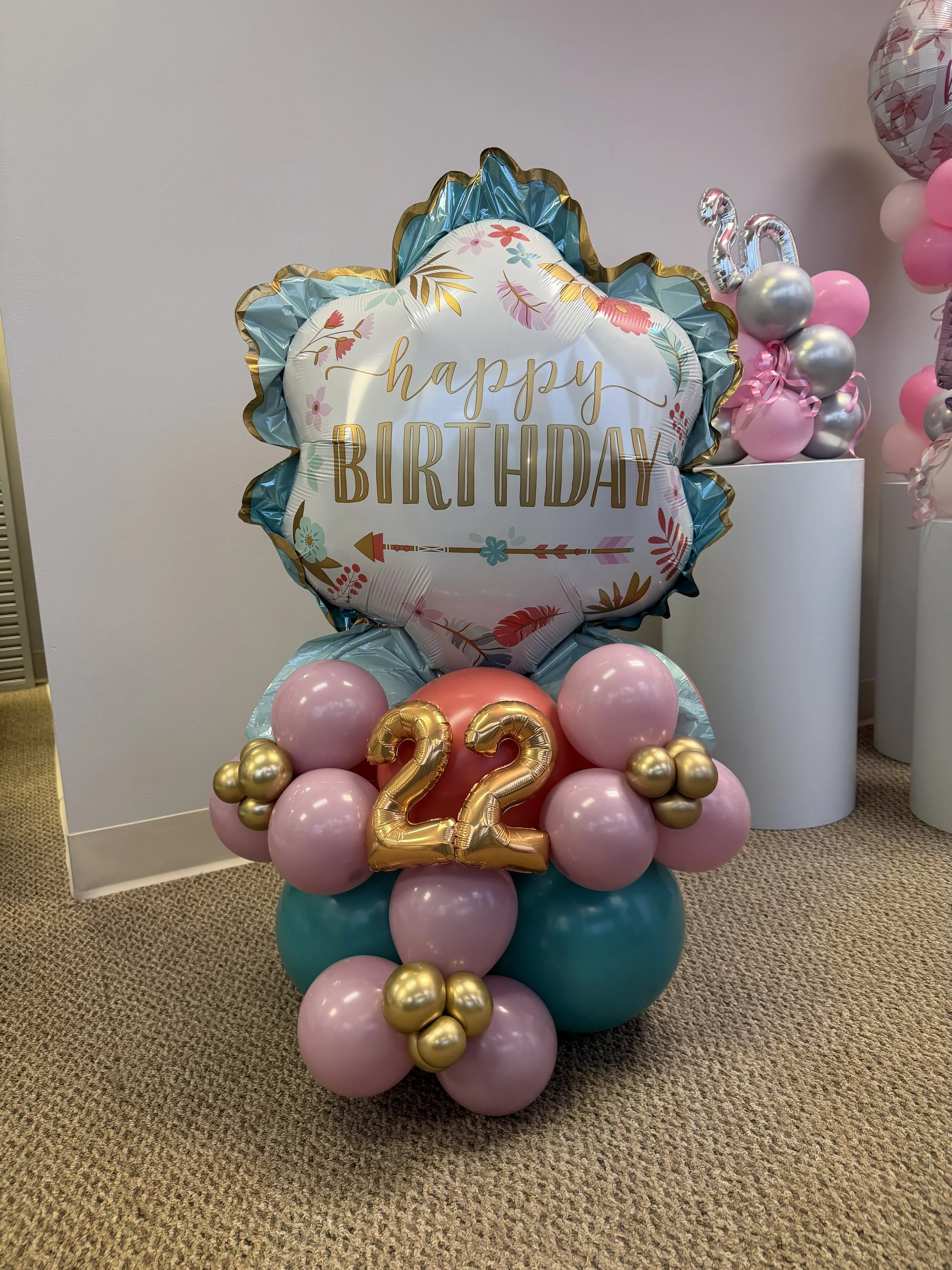 Balloon arrangement with a large 'Happy Birthday' balloon, pink, teal, and gold balloons, and gold number '22' balloons.