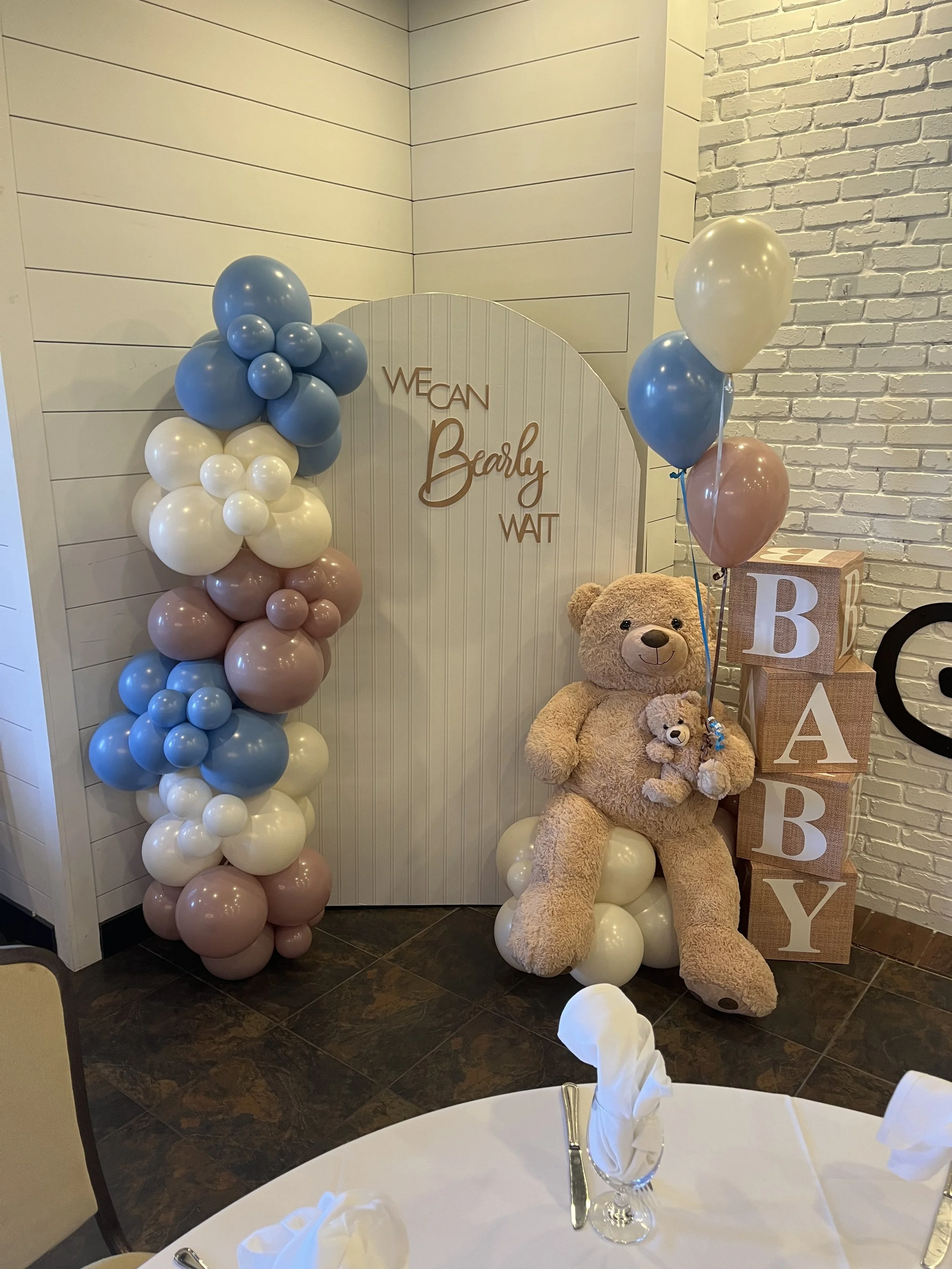 Decorative teddy bear with balloons and baby blocks with the word 'BABY', set for a baby shower celebration.