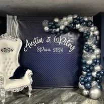 Photo of a decorated backdrop with text, balloons, and a small dog on a white chair, for Austin and Riley's prom 2024.