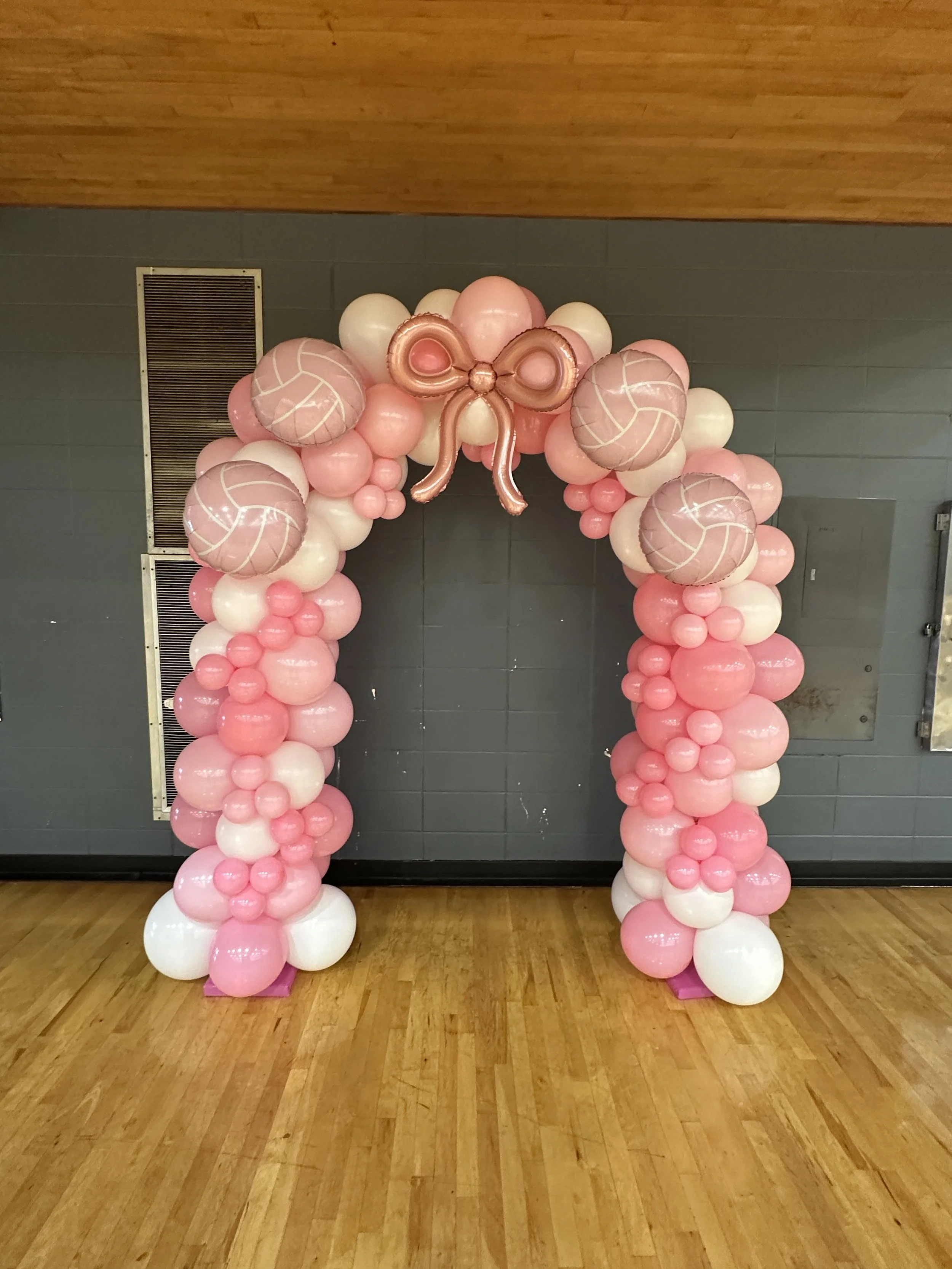 Pink and white balloon arch decorated with a pink bow in the center, suitable for a celebration or party.
