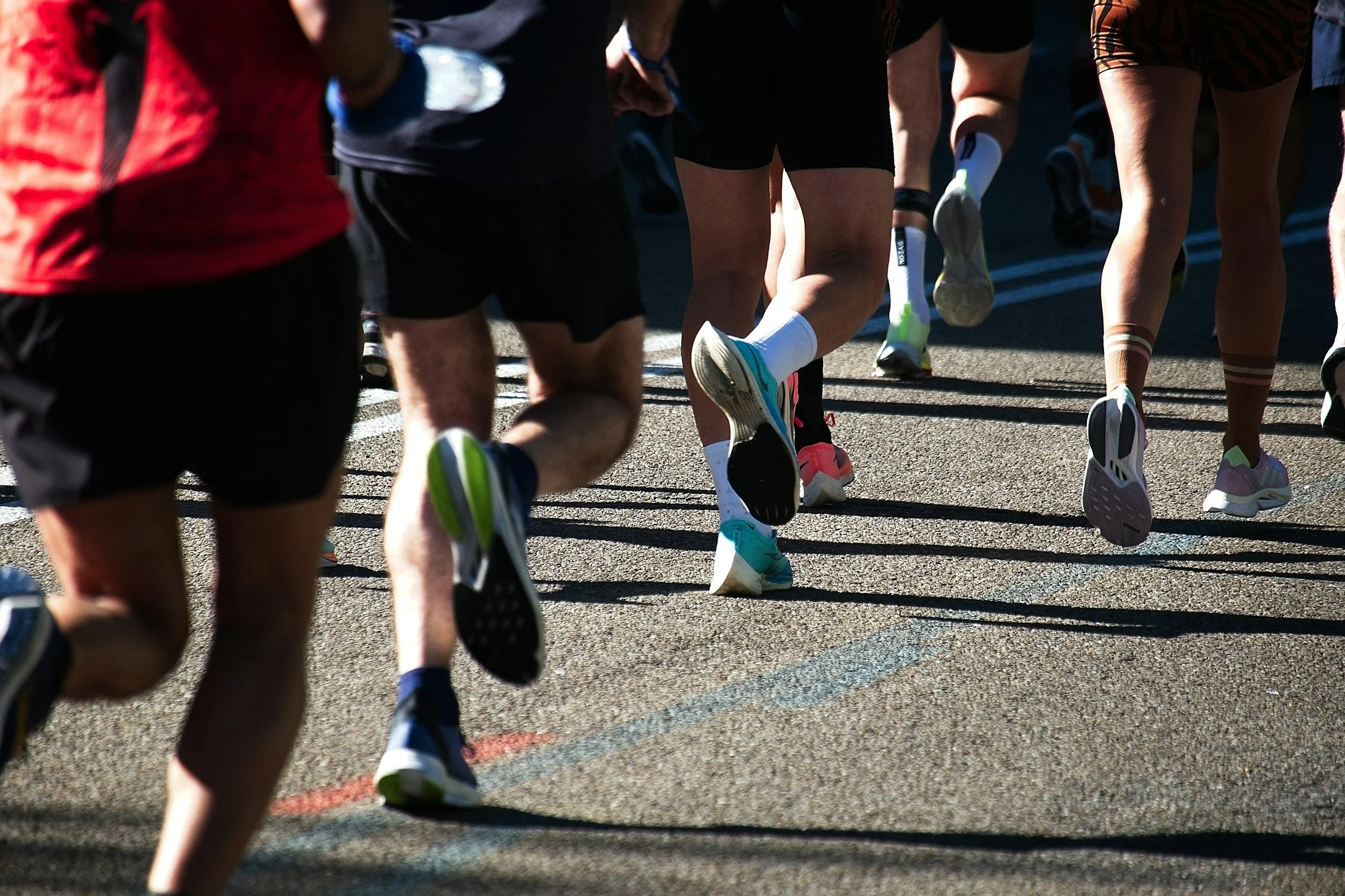 Close-up of runners' legs and feet during a race on a track, with colorful athletic shoes and pavement visible.