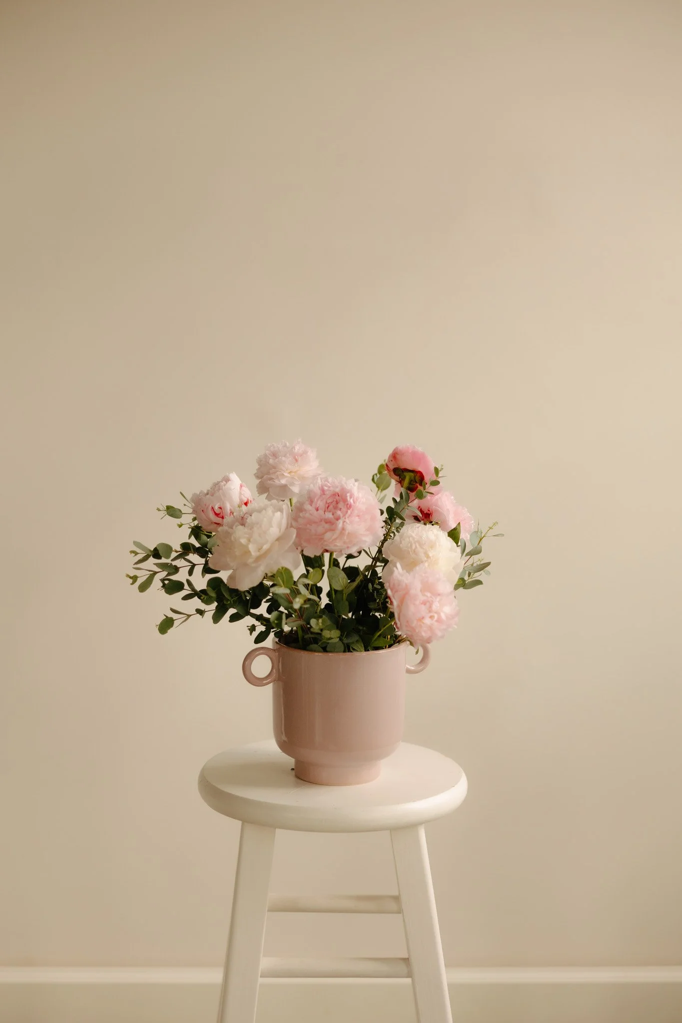 Pink and White peonies arranged in a bowl sitting on a white stool.