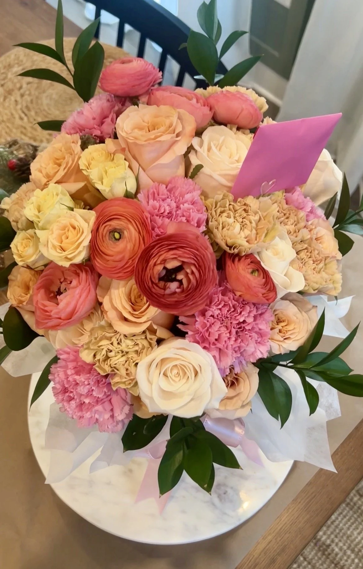 Elevated floral bouquet with assorted coral, pink and cream flowers delicately tied with a pink satin ribbon