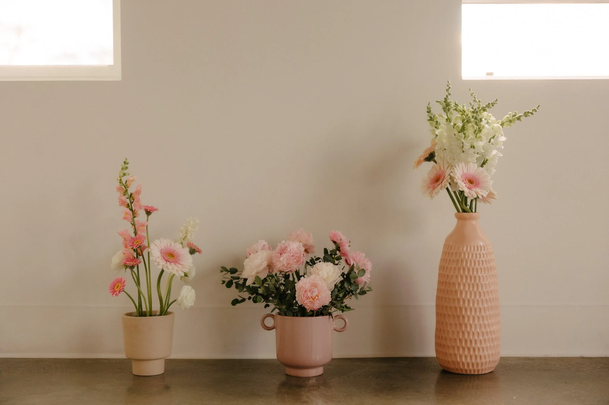3 pink and white flower arrangements on floor sitting under window pane.