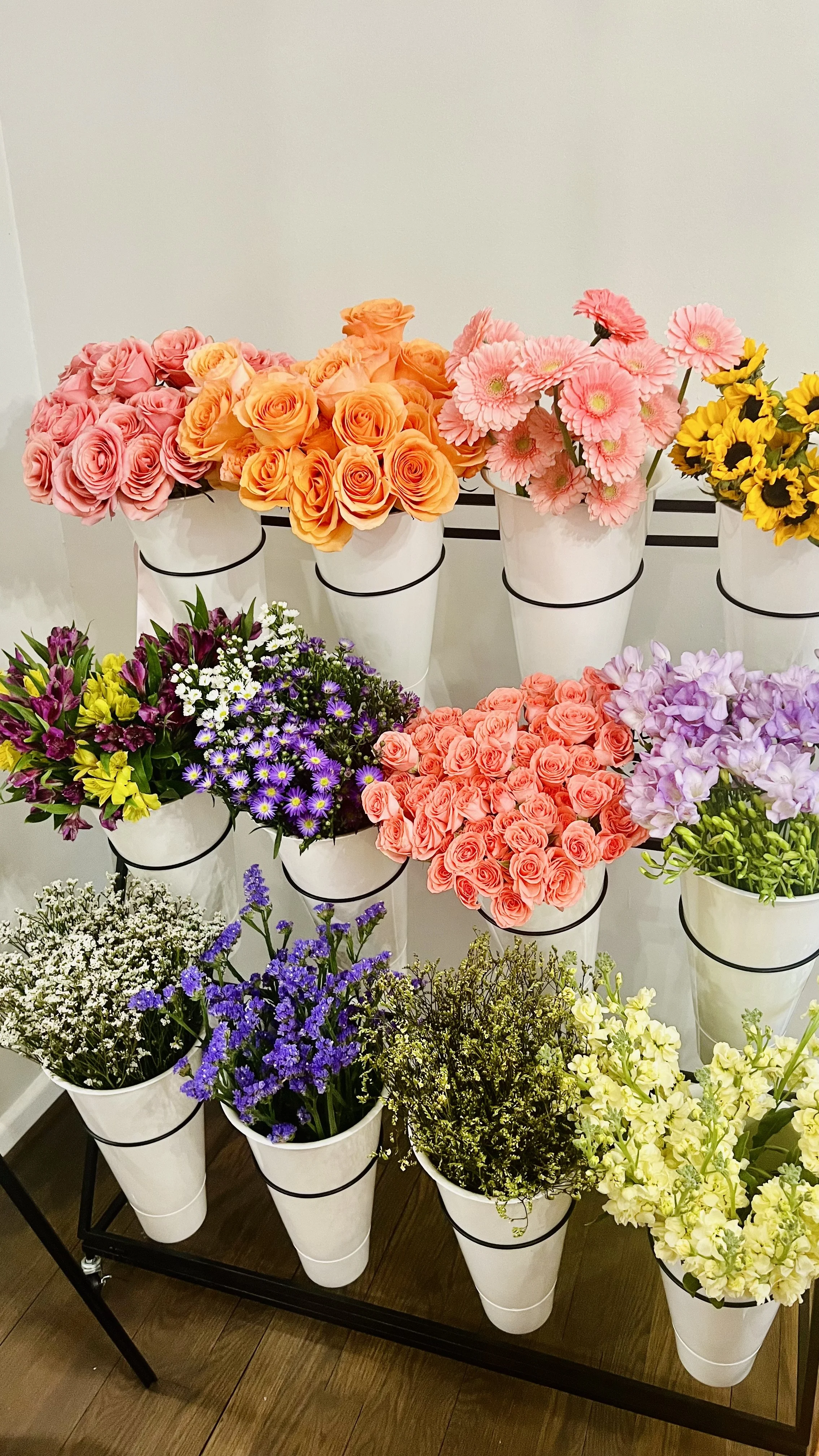 Luxury flower bar display with colorful roses, gerbera daisies, sunflowers, and greenery arranged for a dinner party in white buckets.