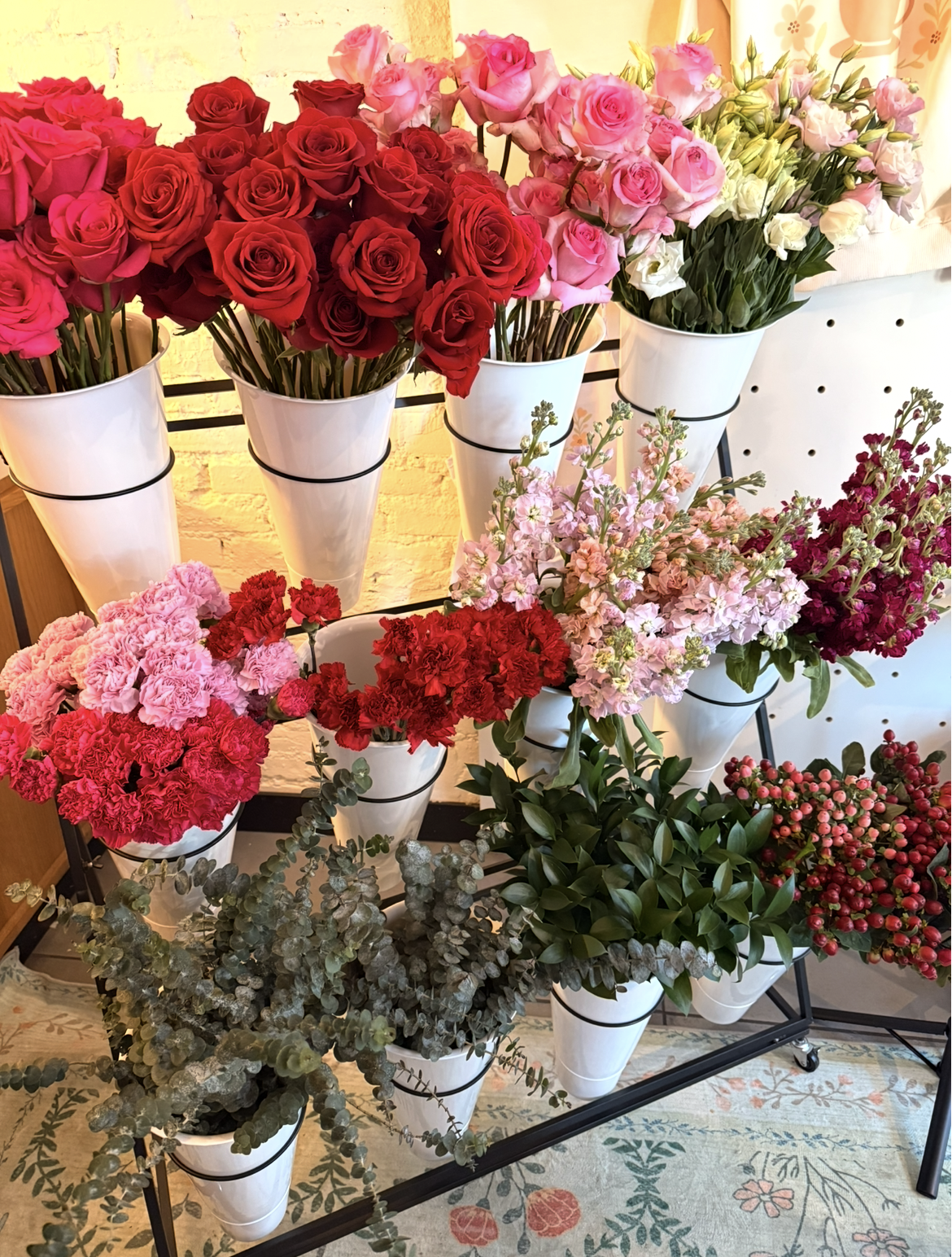 Various pink, red, and white roses and flowers displayed in white pots on a metal stand.