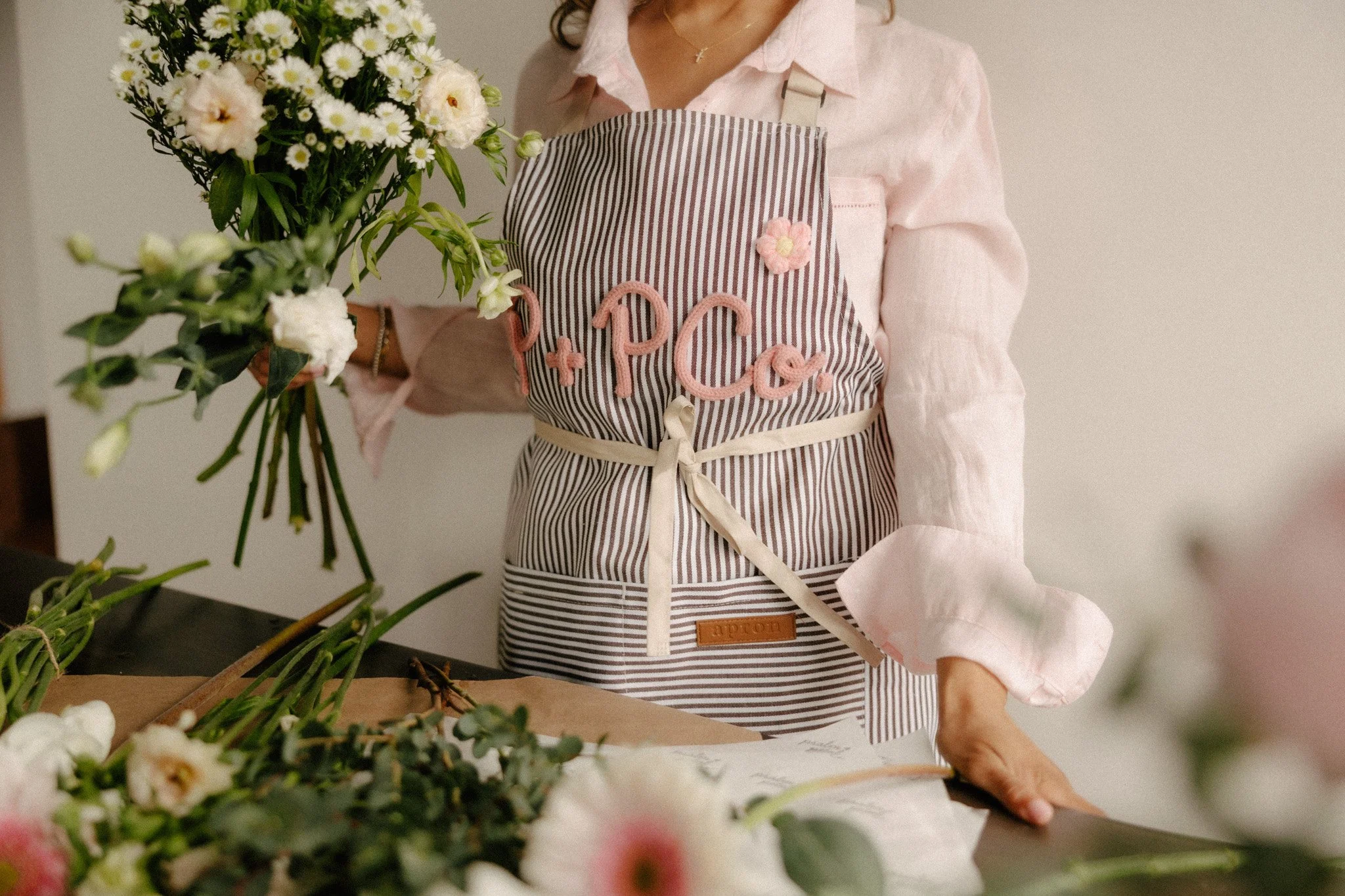 Girl holding variety of white and green flowers wearing a Pink and brown Psalm and Petal Co. apron.