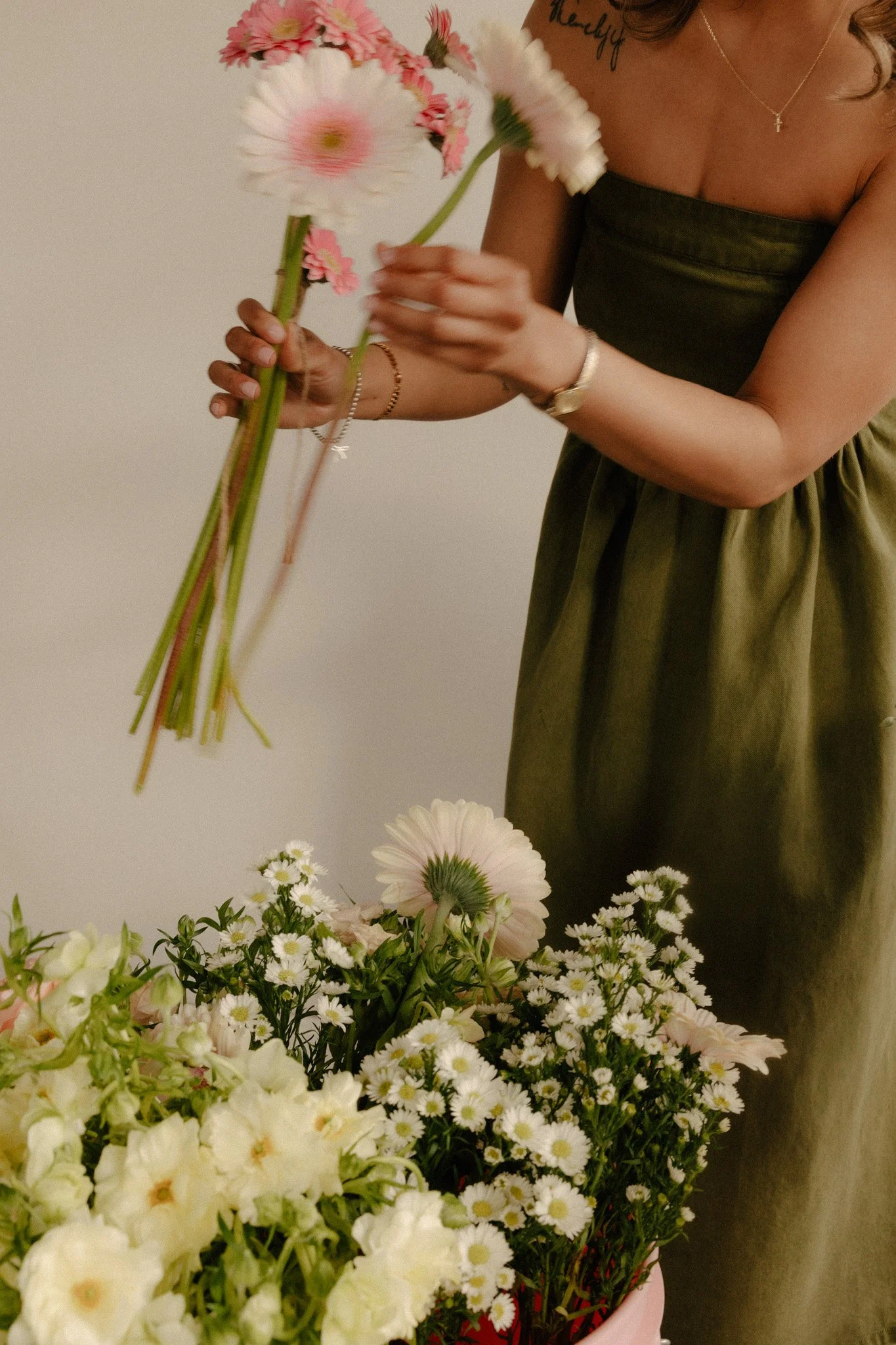 Girl in green dress picking up pink gerbera daisies.