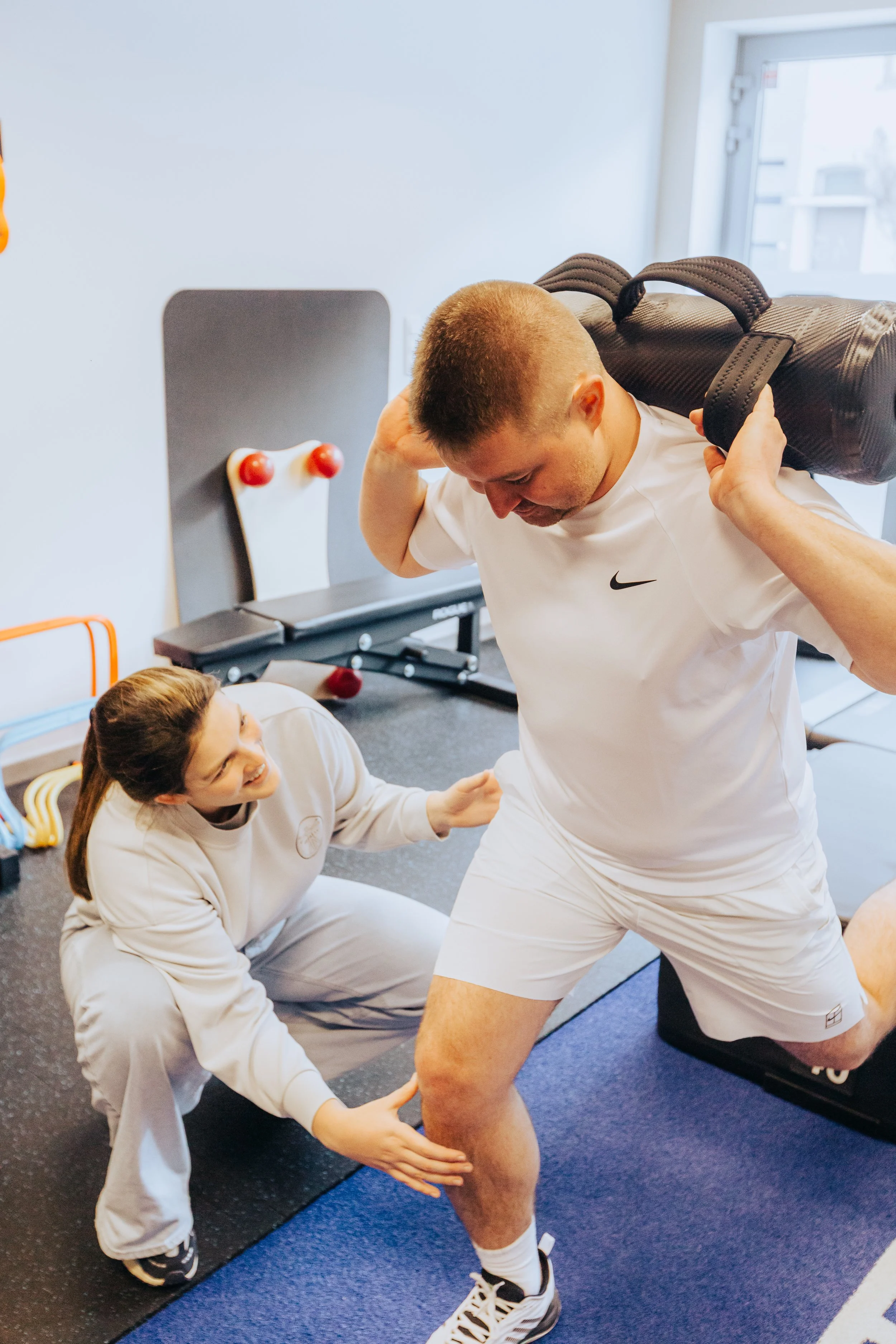 Een man die gewichtheffen doet terwijl een vrouw hem ondersteunt en helpt met de juiste houding, in een fitnessruimte.