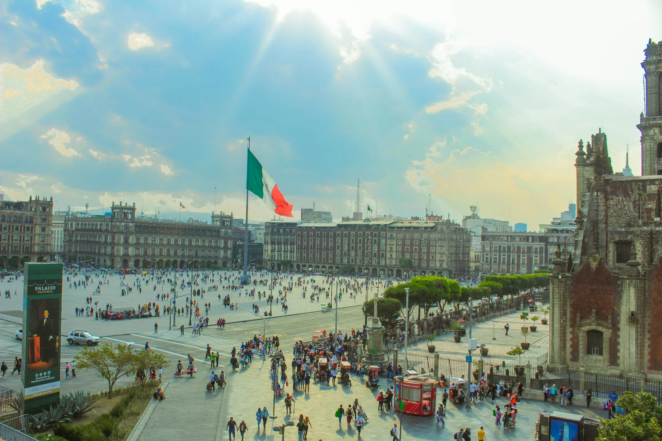 A busy public square with a large Mexican flag on a flagpole.