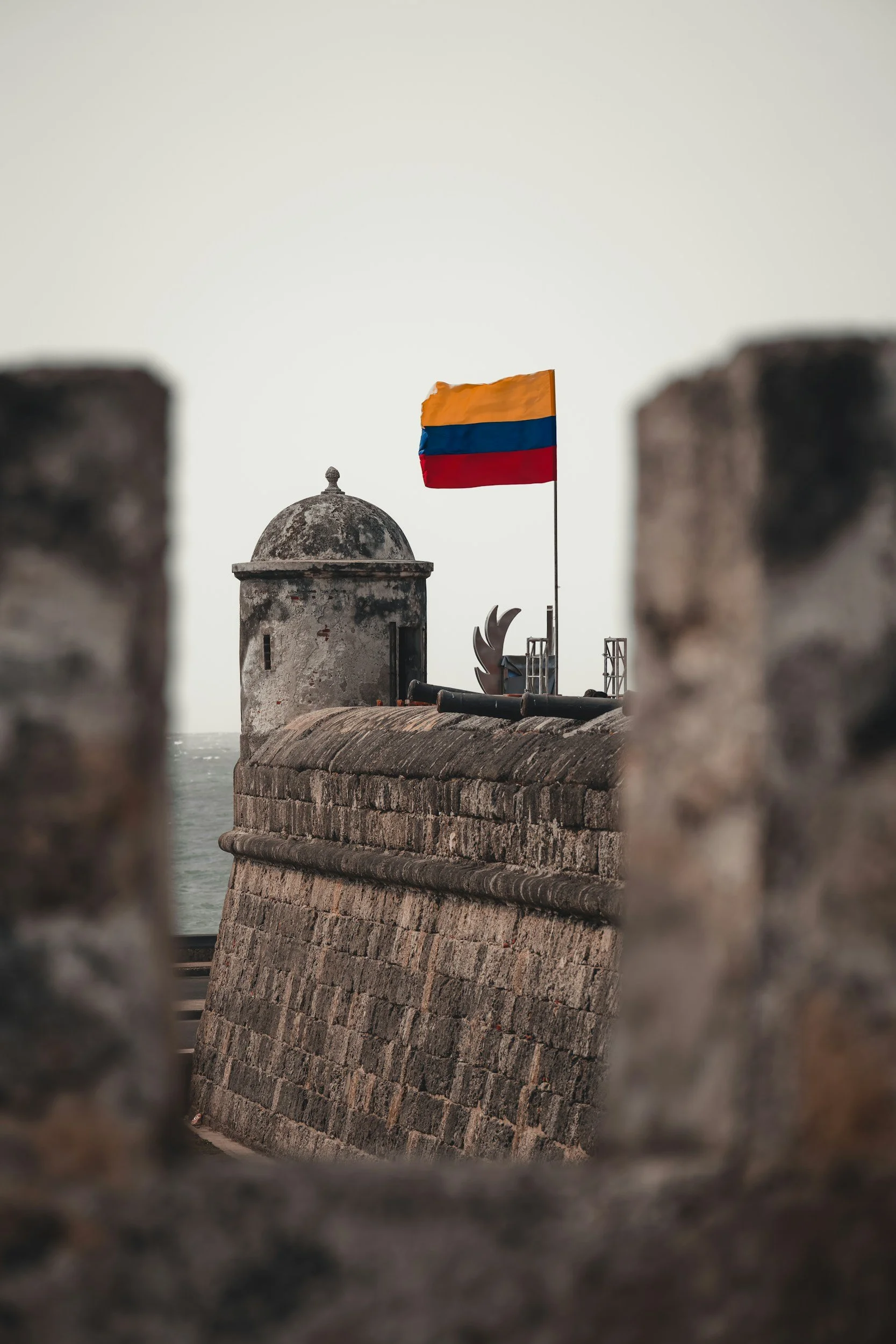 A weathered stone fortification with a large Colombian flag on a flagpole.