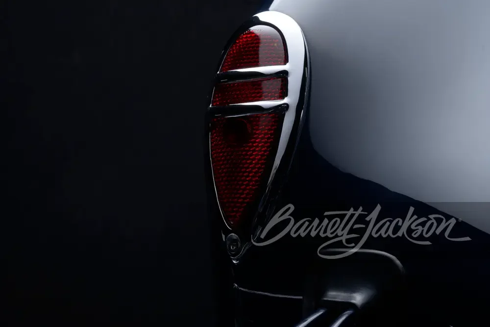 Close-up of a vintage motorcycle tail light and part of the white body, with a dark background.