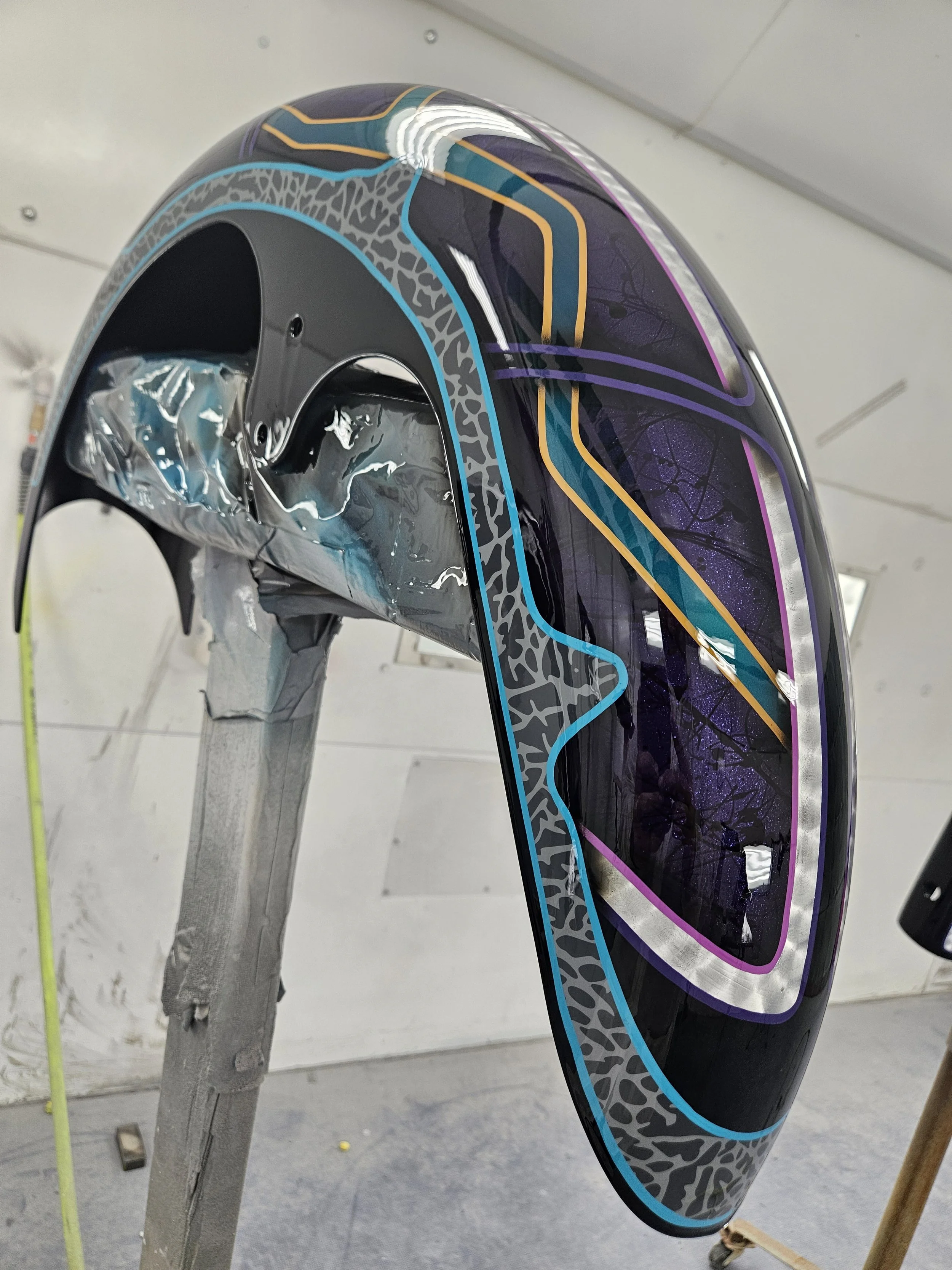 Close-up of a large, colorful, artistic sculpture or installation with black, purple, and yellow design elements and a protective plastic cover, set indoors.