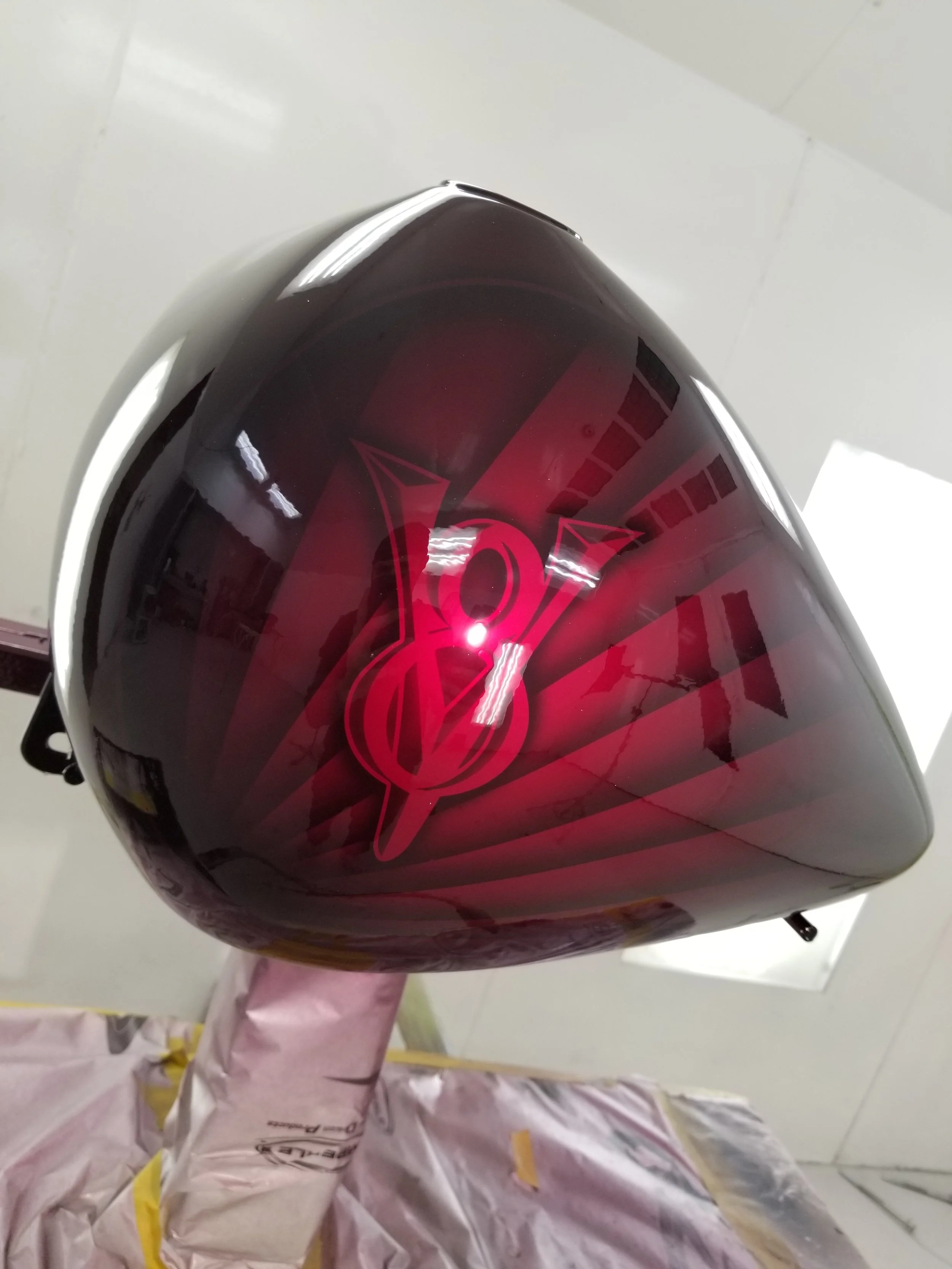 A maroon custom painted motorcycle part with a red logo and design, placed on a stand covered with protective paper.