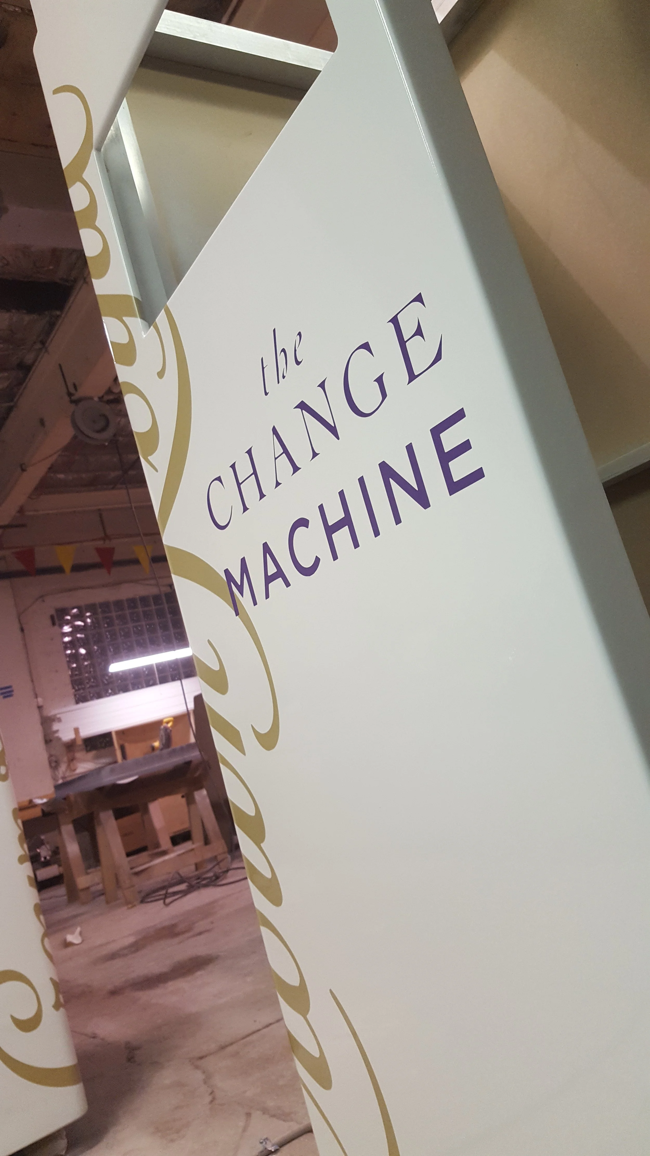 A white sign with gold decorative accents and purple text that reads 'the CHANGE MACHINE'.