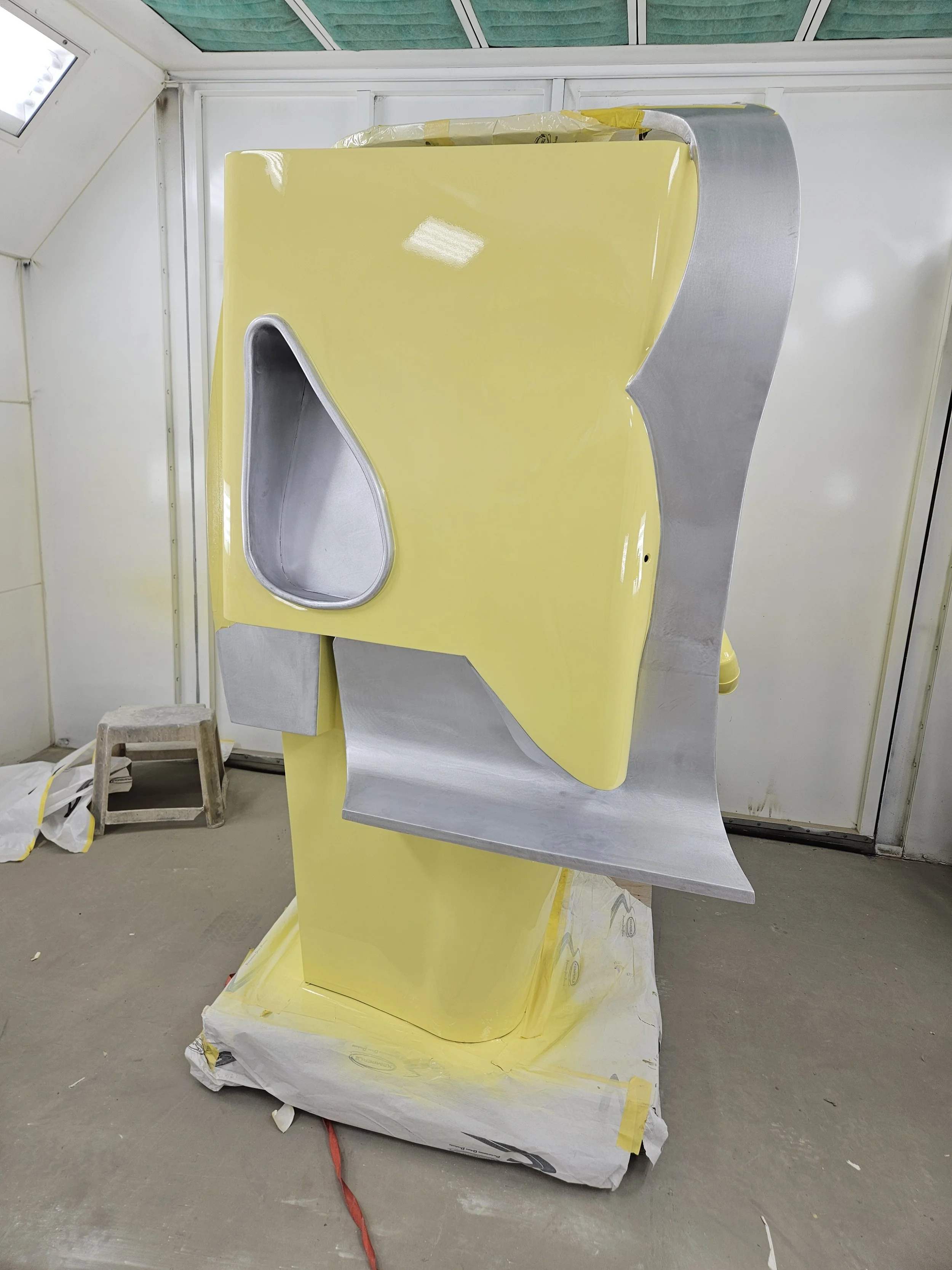 A partially painted yellow and gray vintage jukebox in a paint booth.