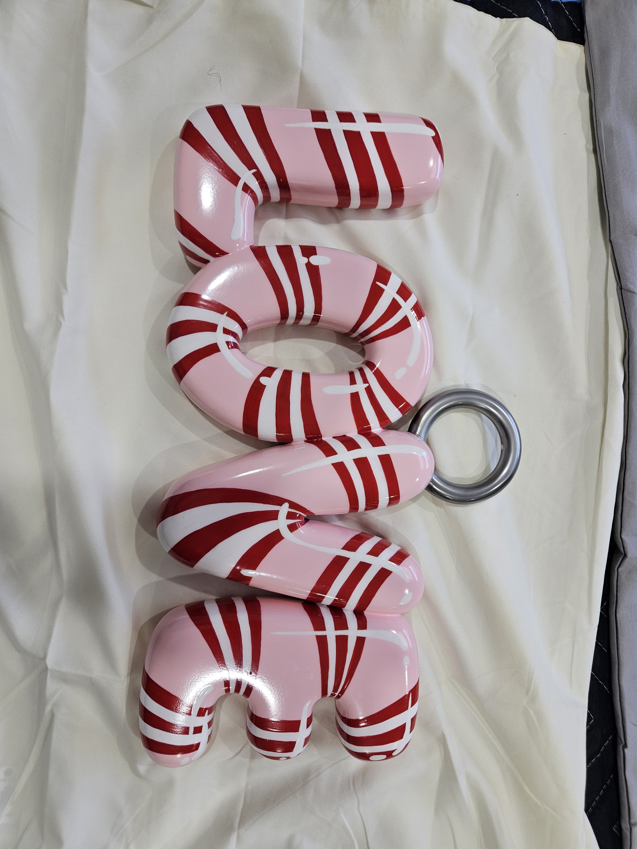 Decorative holiday sign spelling the word "LOVE" in pink with red and white striped accents, with a silver ring attached to the last letter.