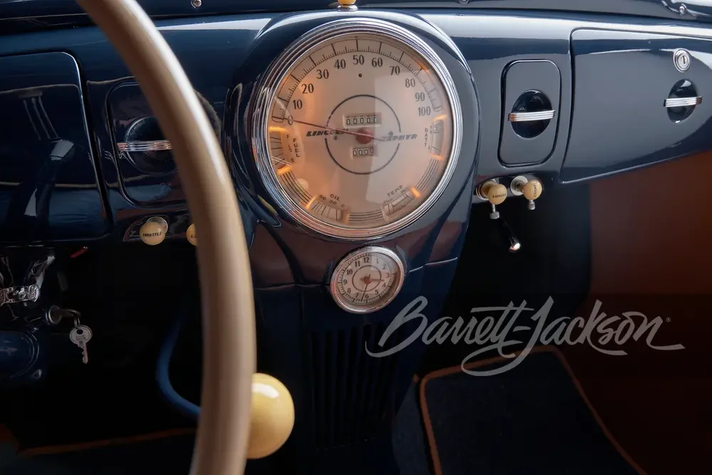 Close-up of vintage car dashboard with large speedometer, smaller clock, and radio controls, featuring Barrett-Jackson logo.