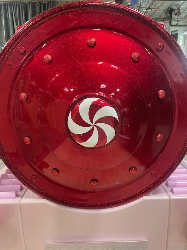 Red cylindrical object with evenly spaced bolts and a black and white swirled spiral inside at the bottom.